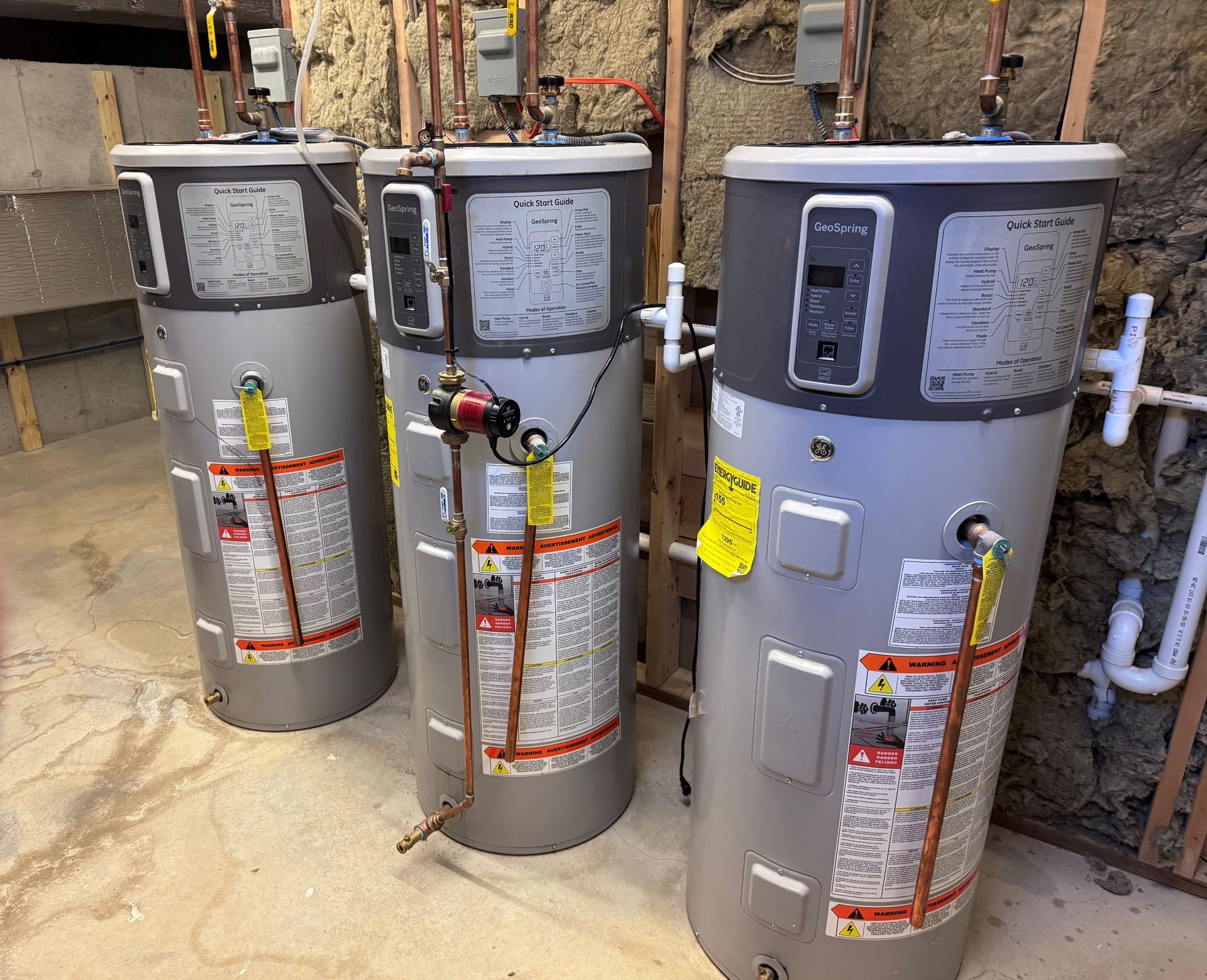 Three water heaters are sitting next to each other in a basement.