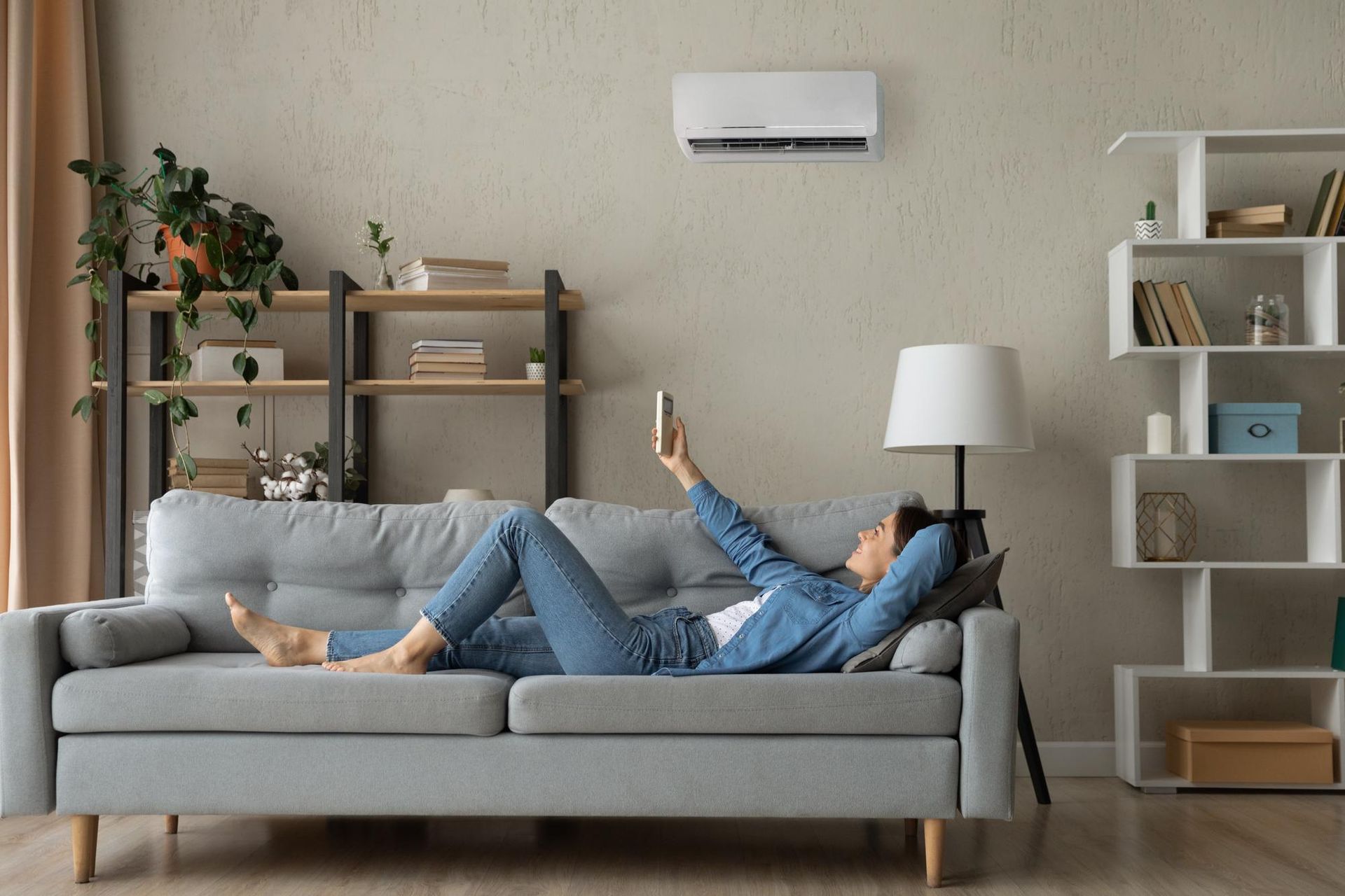 A woman is laying on a couch in a living room using a tablet.