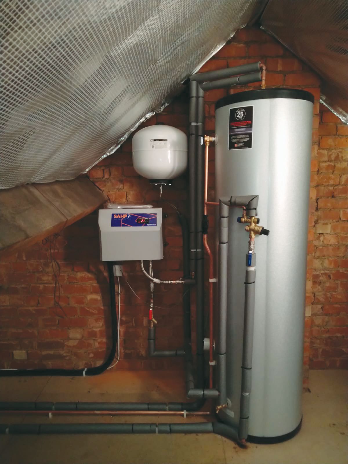 A water heater is sitting in a room next to a brick wall.