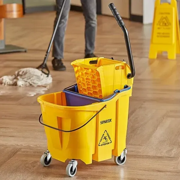 A yellow mop bucket with wheels is on a wooden floor.