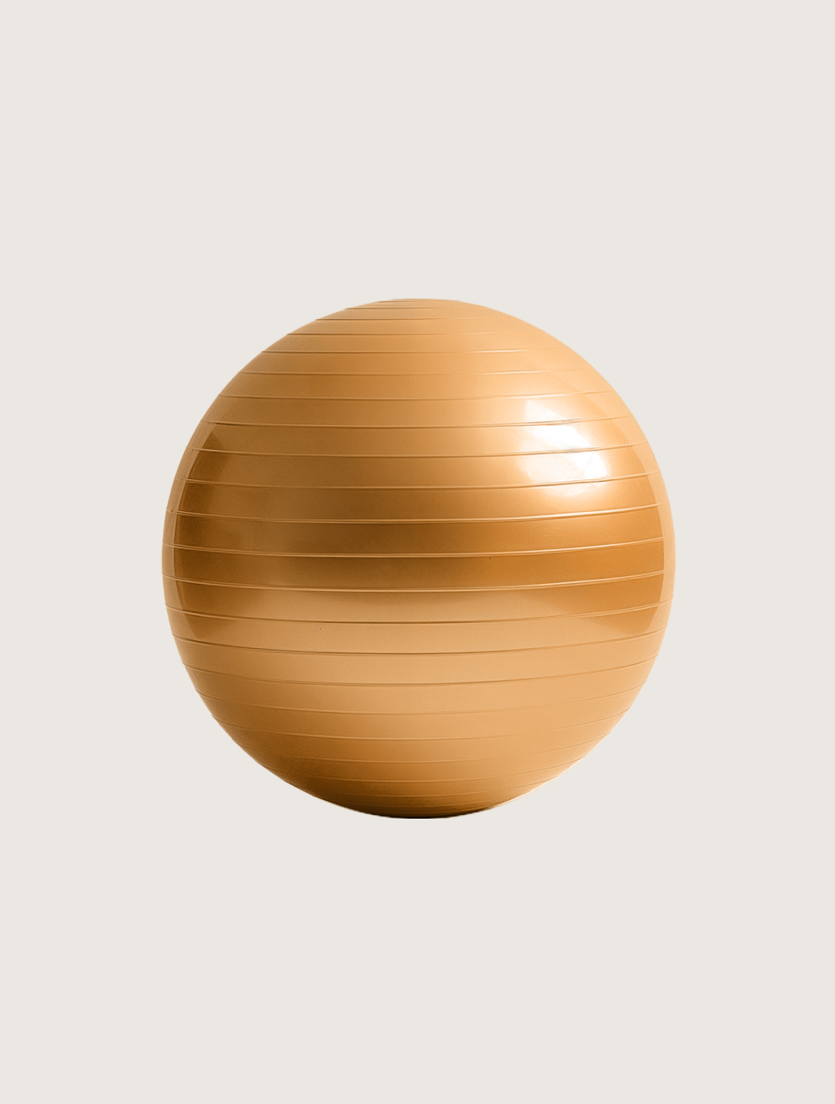 A gold exercise ball is sitting on a white surface.