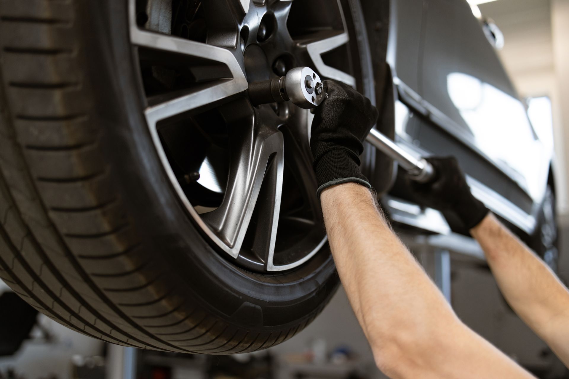 Mechanic tightening a lug nut on a car tire with a wrench, wearing gloves, in a garage.