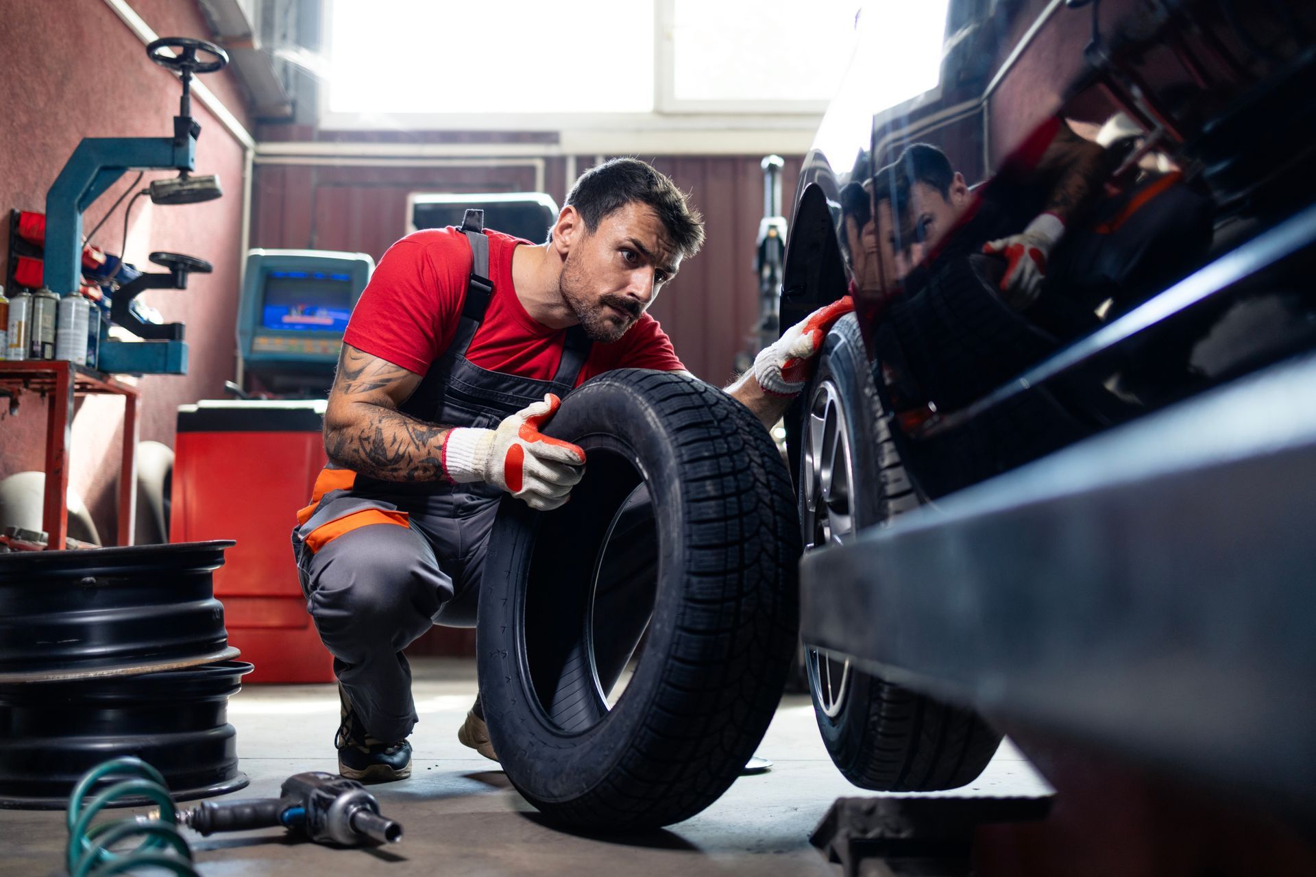 Mechanic in red shirt and gloves, changing a tire in a garage.