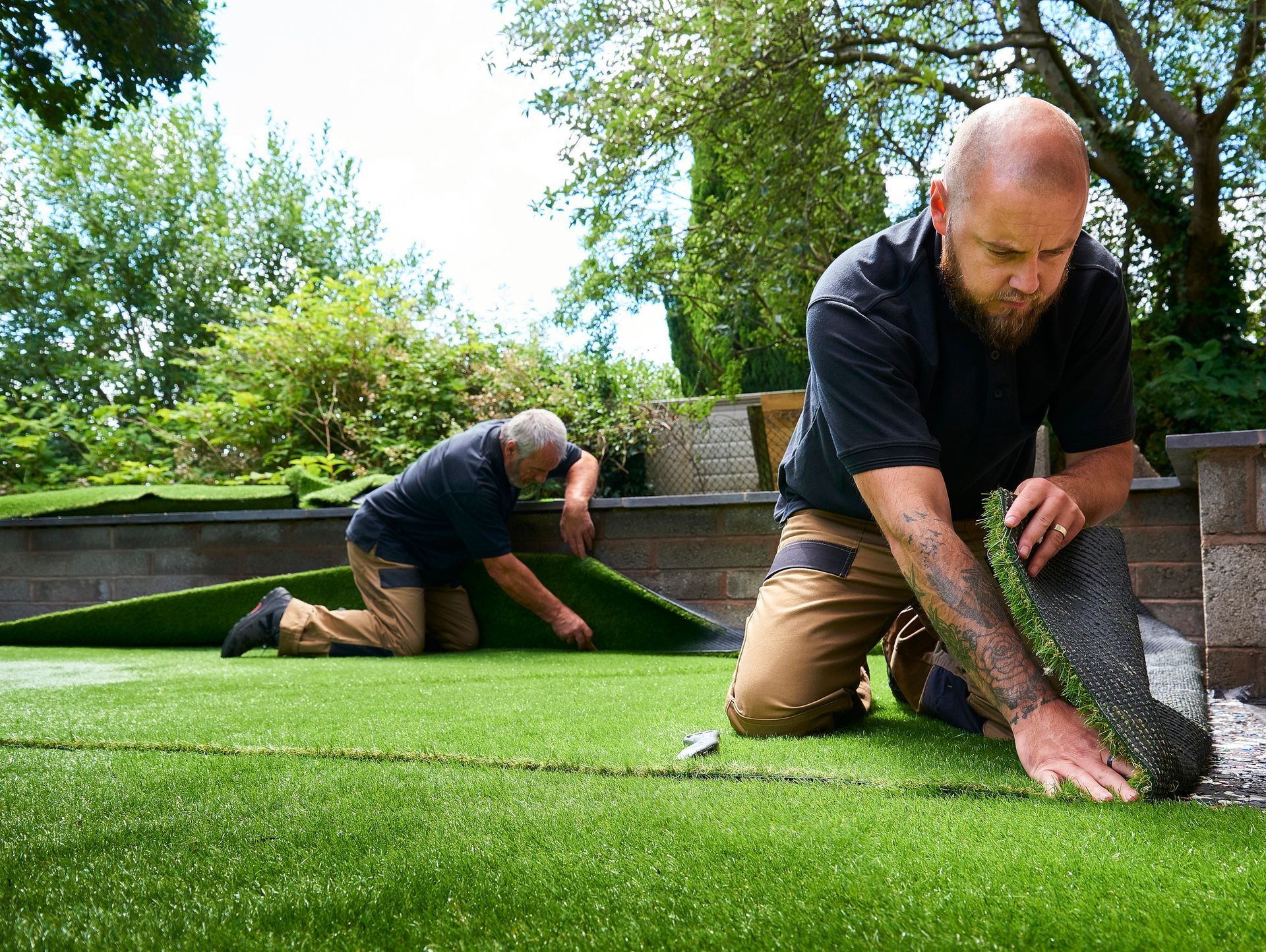 Two men are installing artificial grass in a backyard.