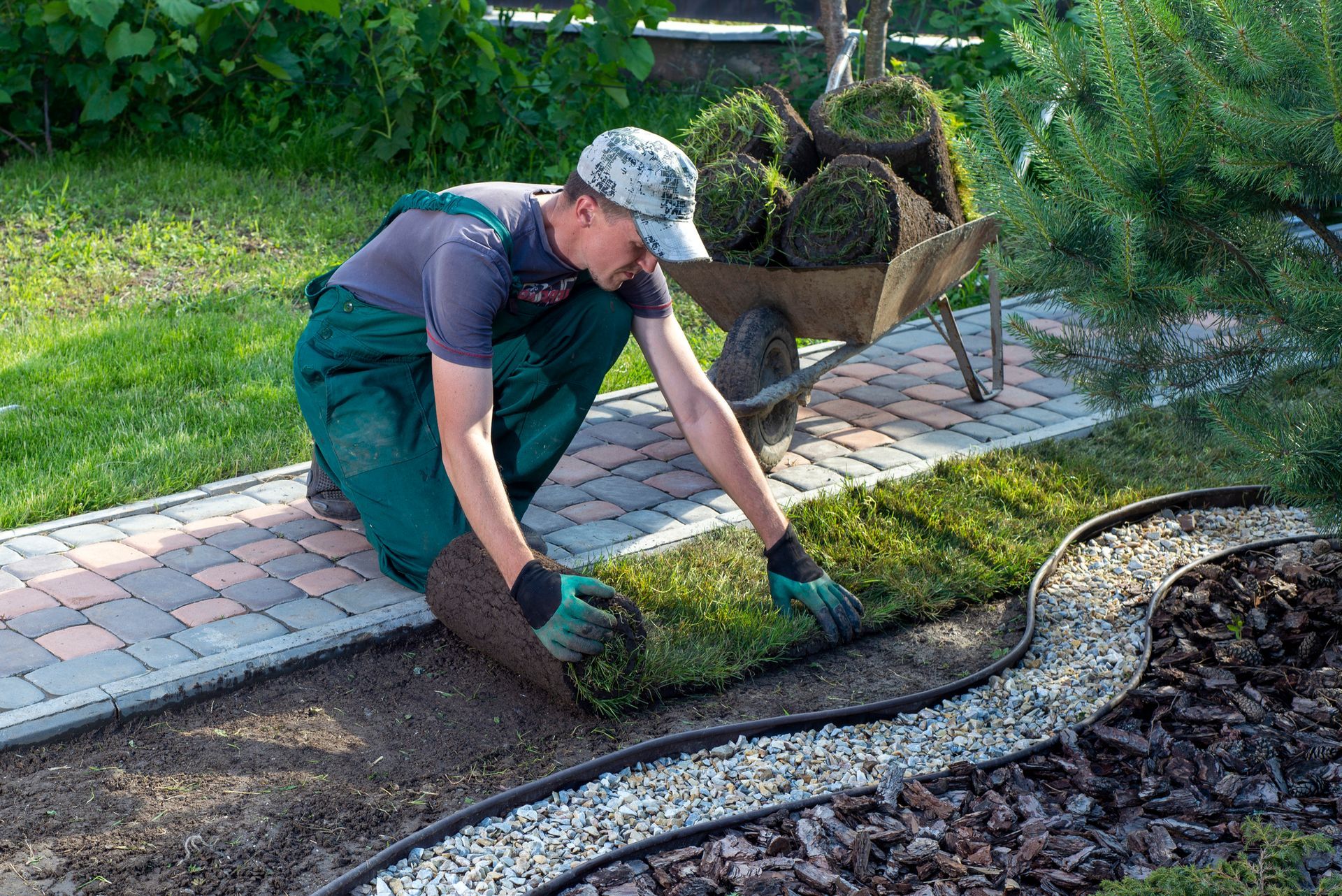 A man is laying a roll of grass in a garden.