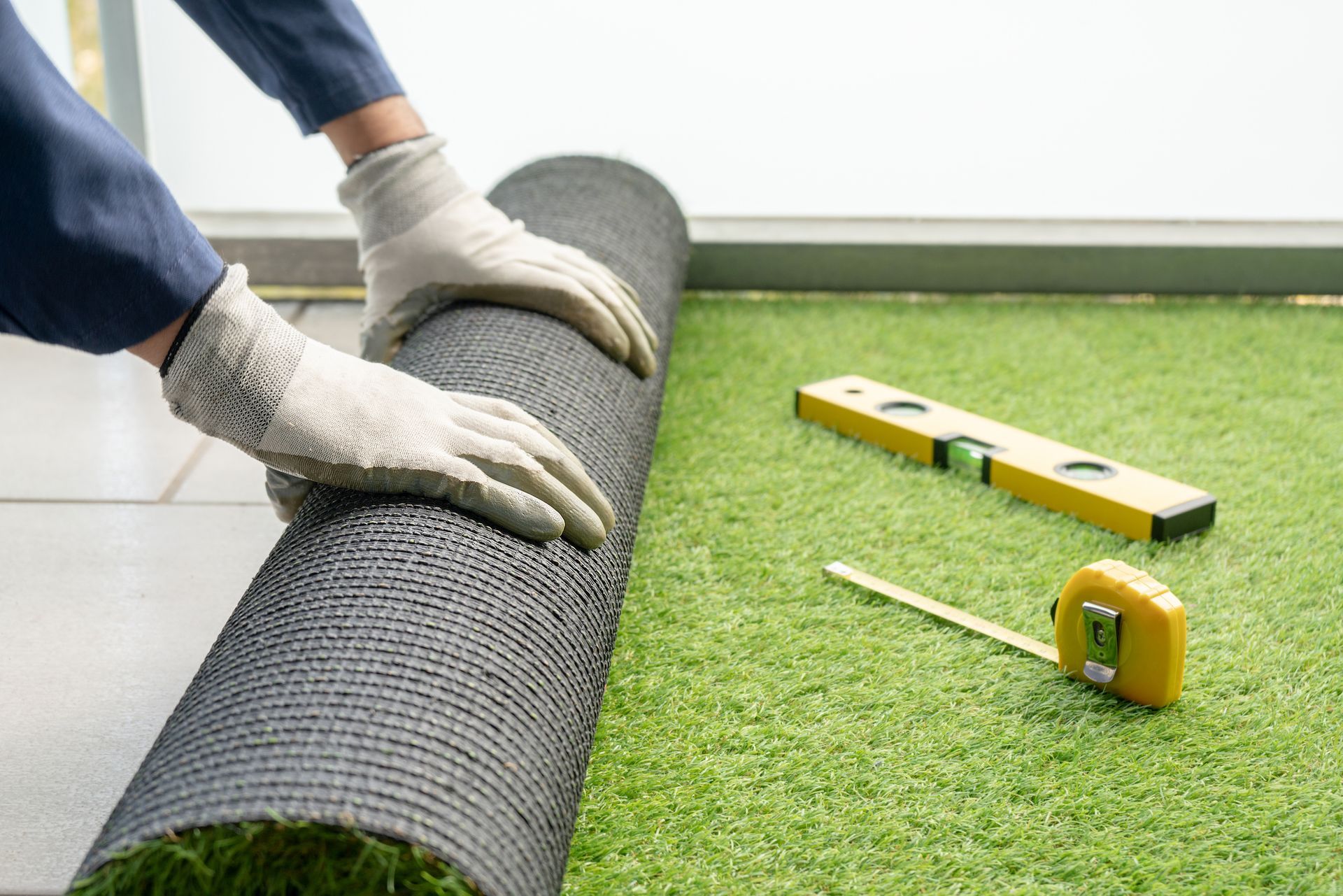 A person is rolling a roll of artificial grass on the floor.