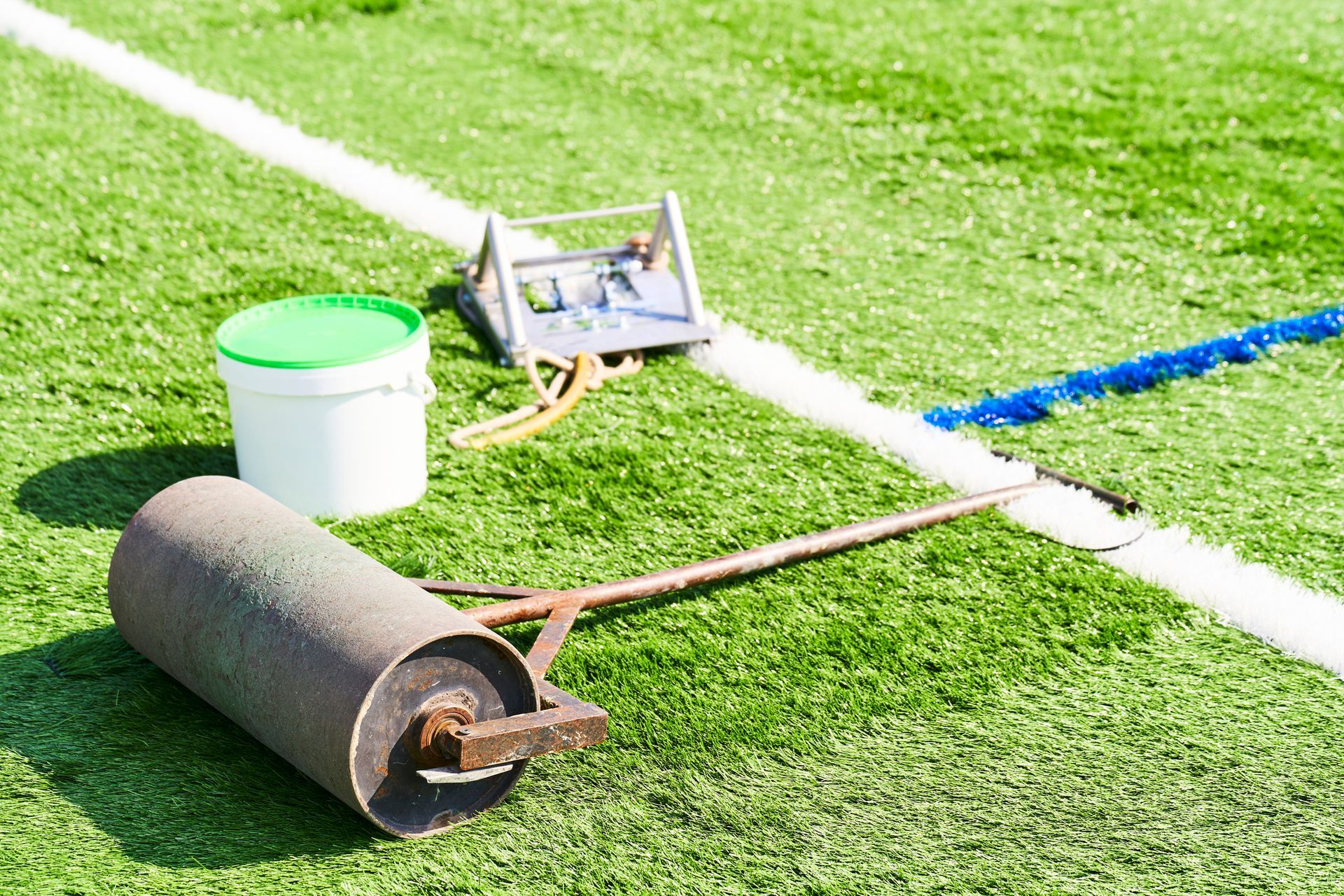A roller is sitting on top of a soccer field next to a bucket.