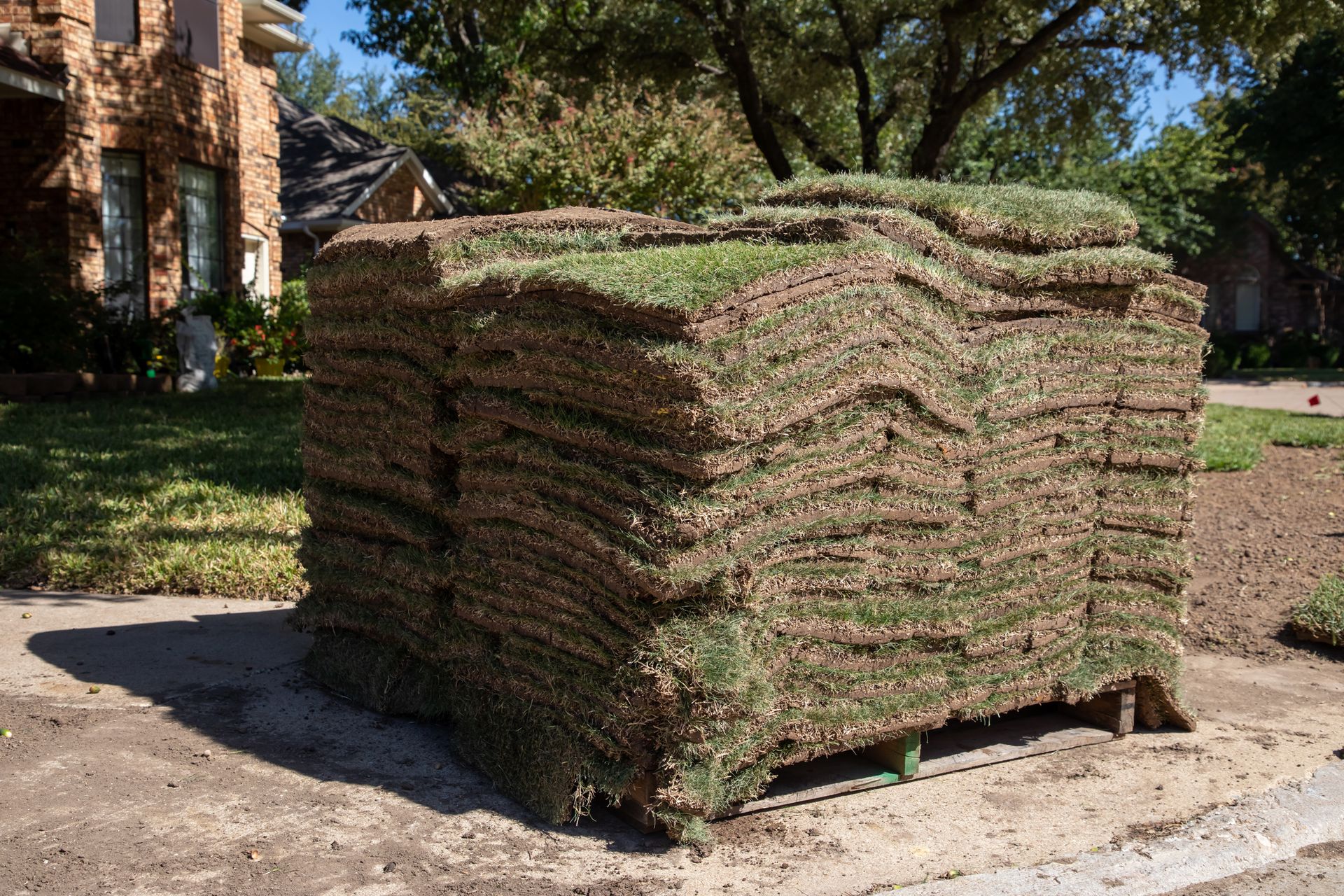 A large stack of sod is sitting on the side of the road in front of a house.