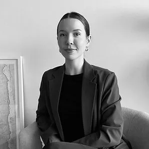 A black and white photo of a woman in a suit sitting in a chair.