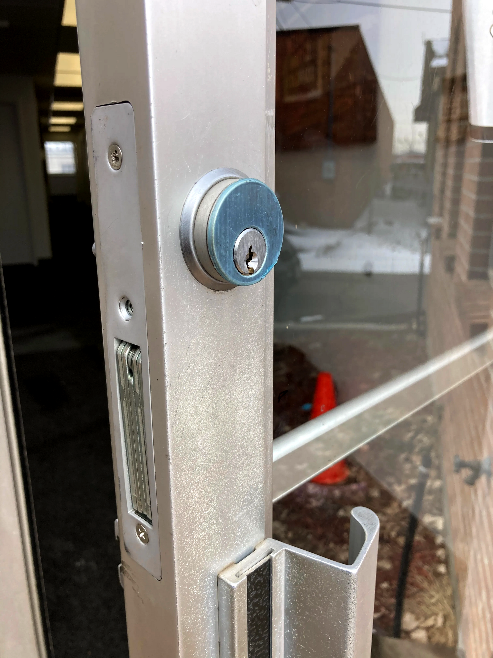 Close-up of a blue deadbolt lock and glass door handle on a metal-framed door