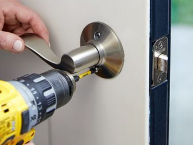 Hand installing a silver door lever with a drill on a white door.