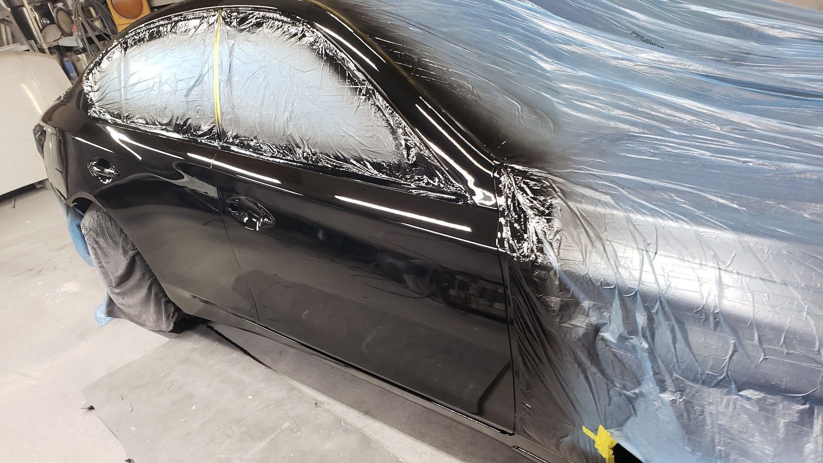 Black car door and window masked with plastic and tape in a body shop during painting