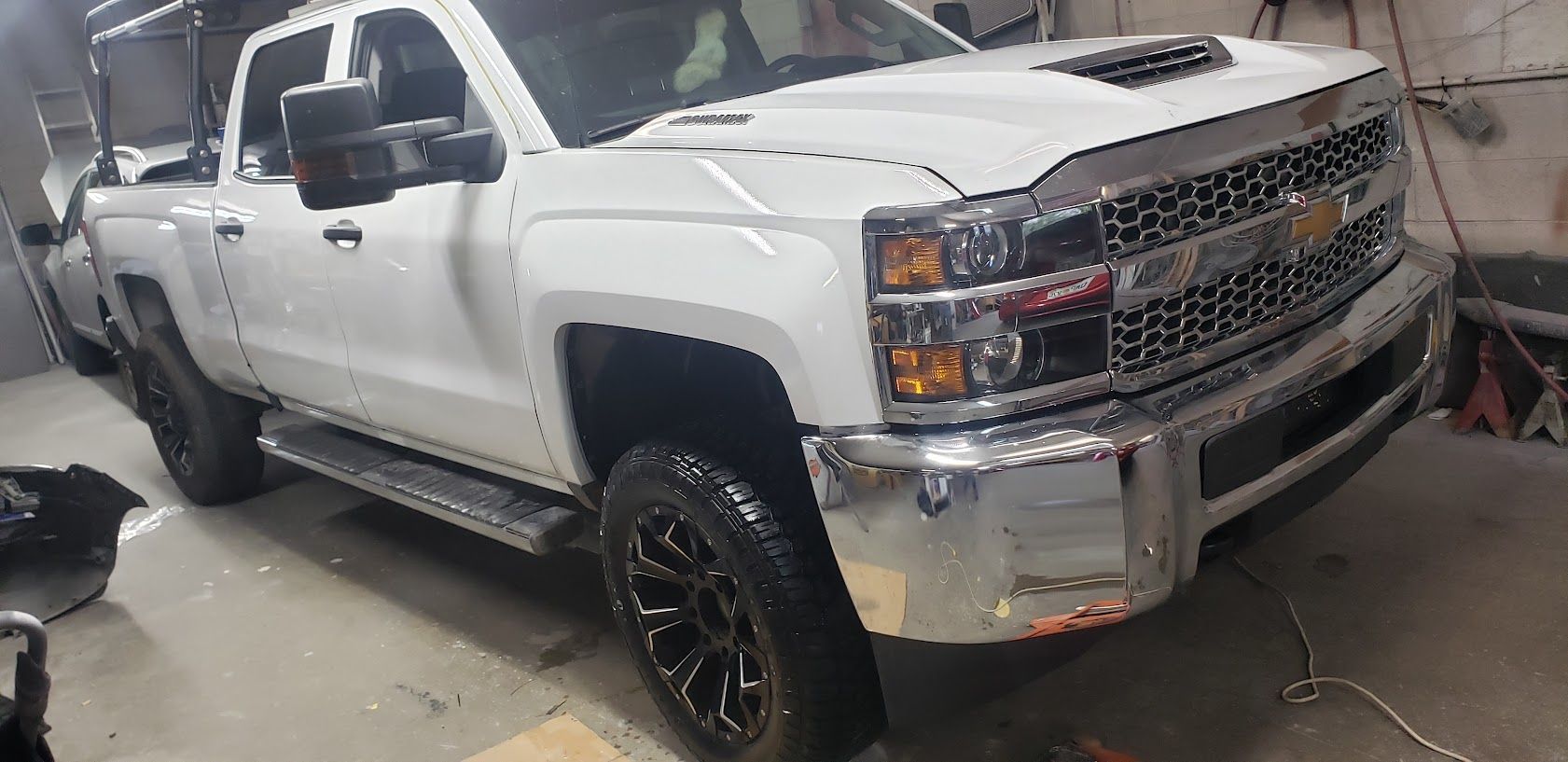 White lifted pickup truck in a garage, shown from the front-left side.