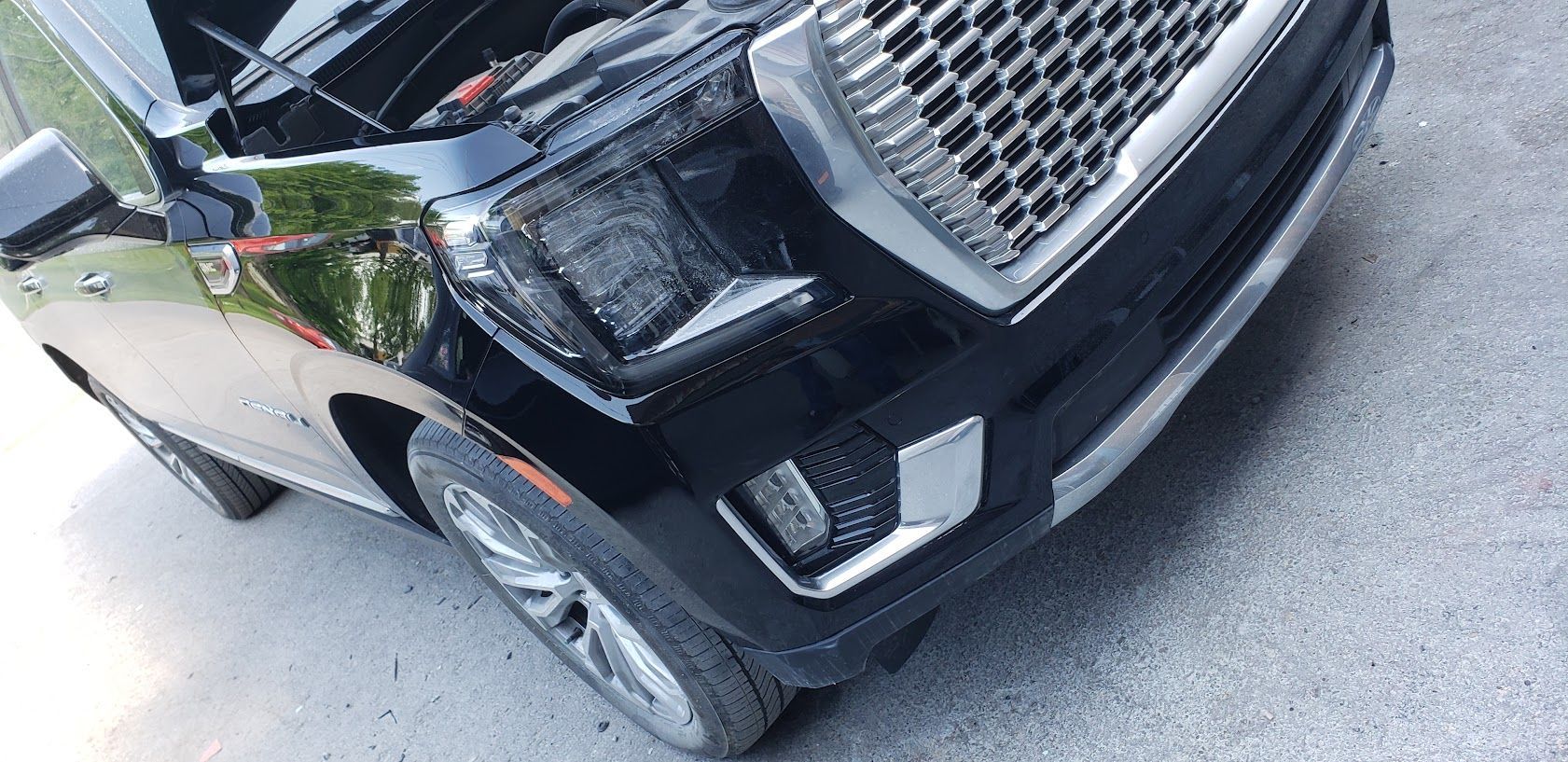 Black SUV with damaged front bumper and grille, parked on a street near a curb.