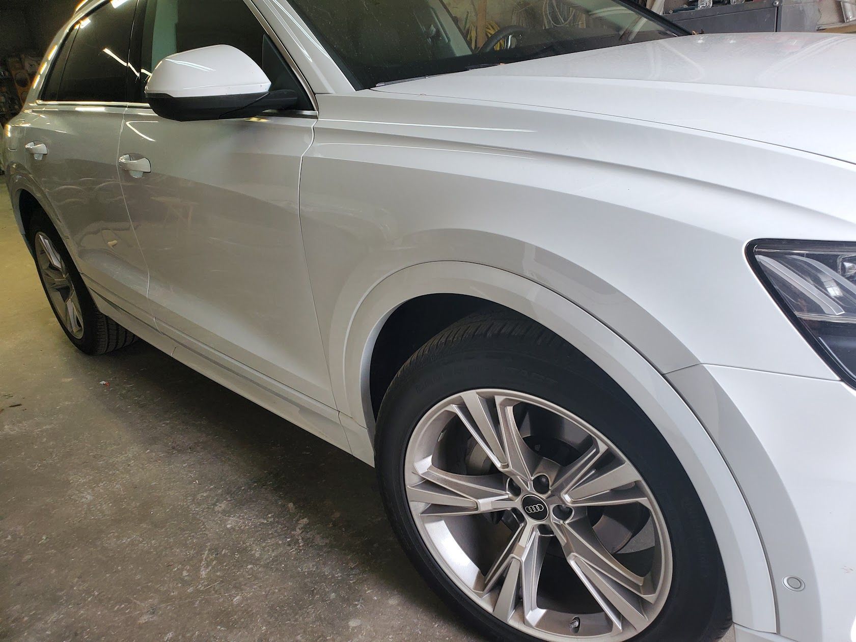 White SUV parked indoors, side view showing front wheel and chrome trim.