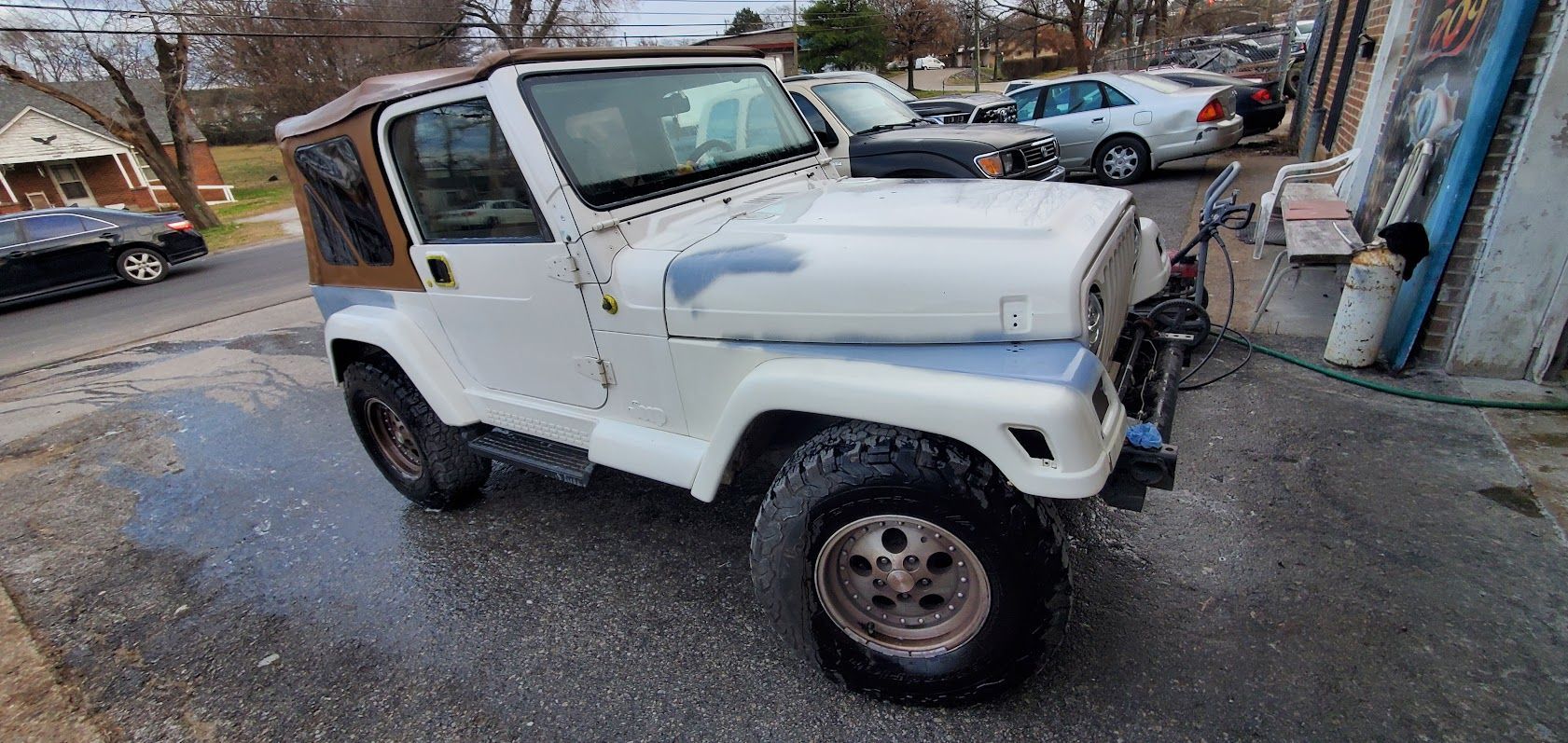 White off-road SUV parked on a street beside a building, with other cars in the background.