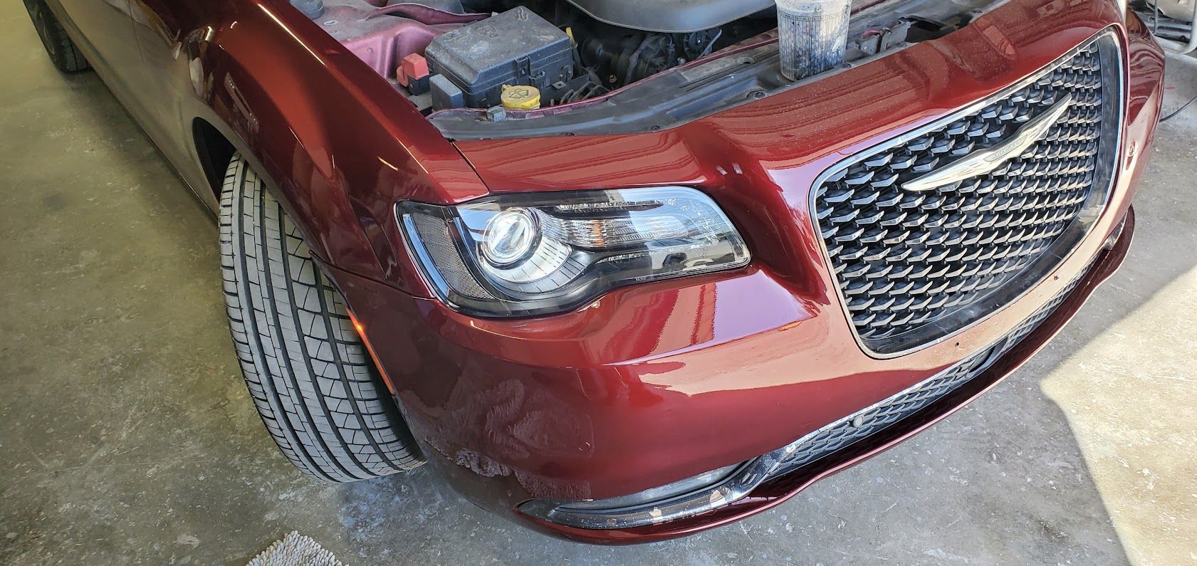 Red Chrysler sedan with hood open, front-left view in a driveway