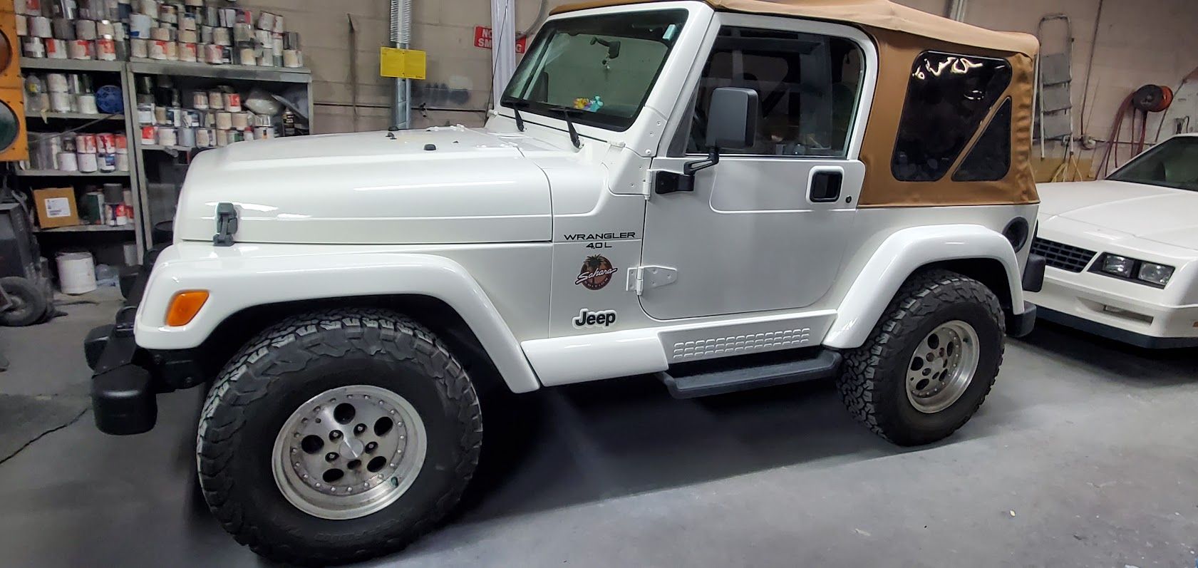 White Jeep Wrangler parked indoors in a garage, with a black soft top and off-road tires