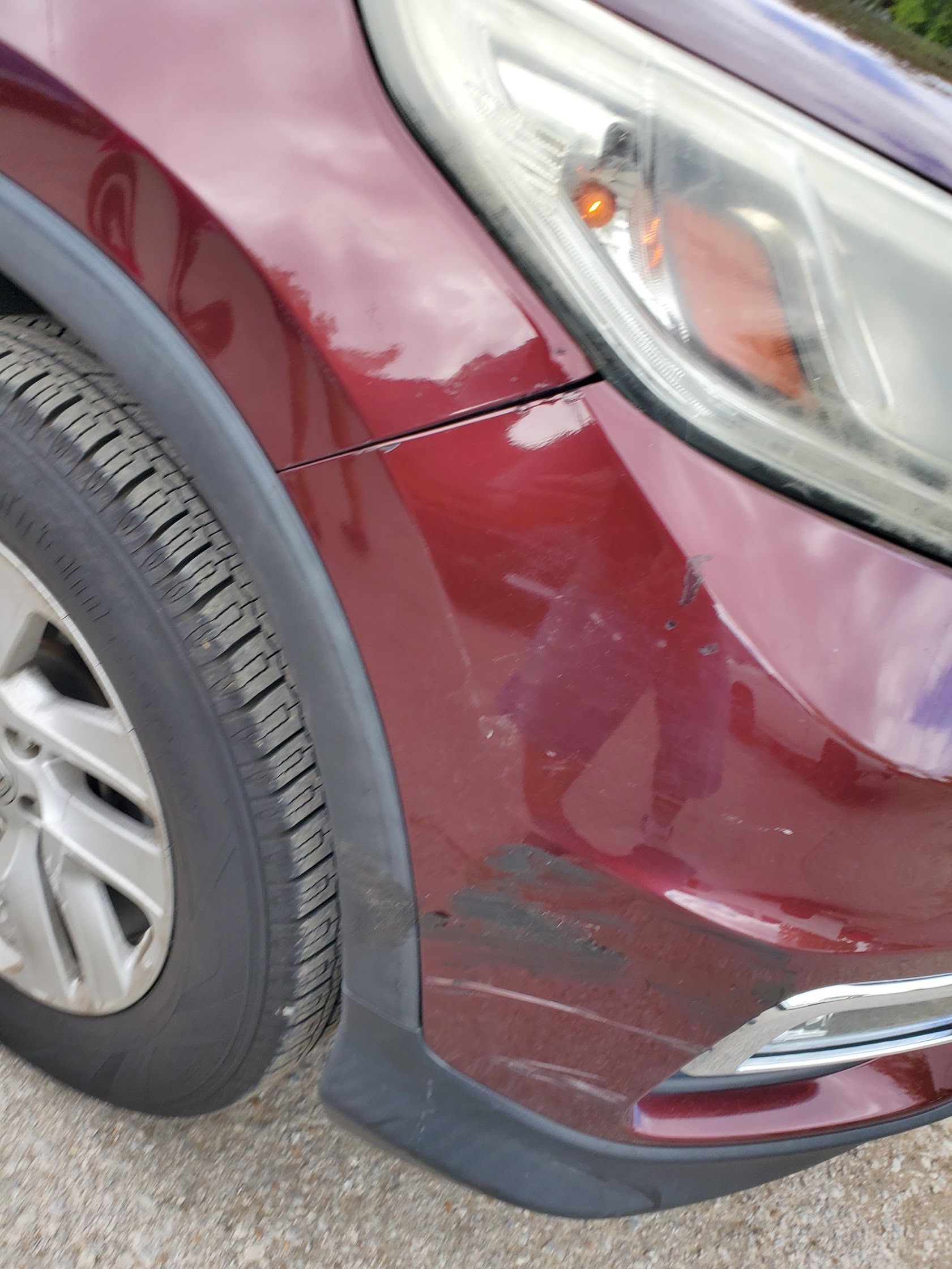 Maroon car’s front-left corner with scrape damage near the bumper and wheel well