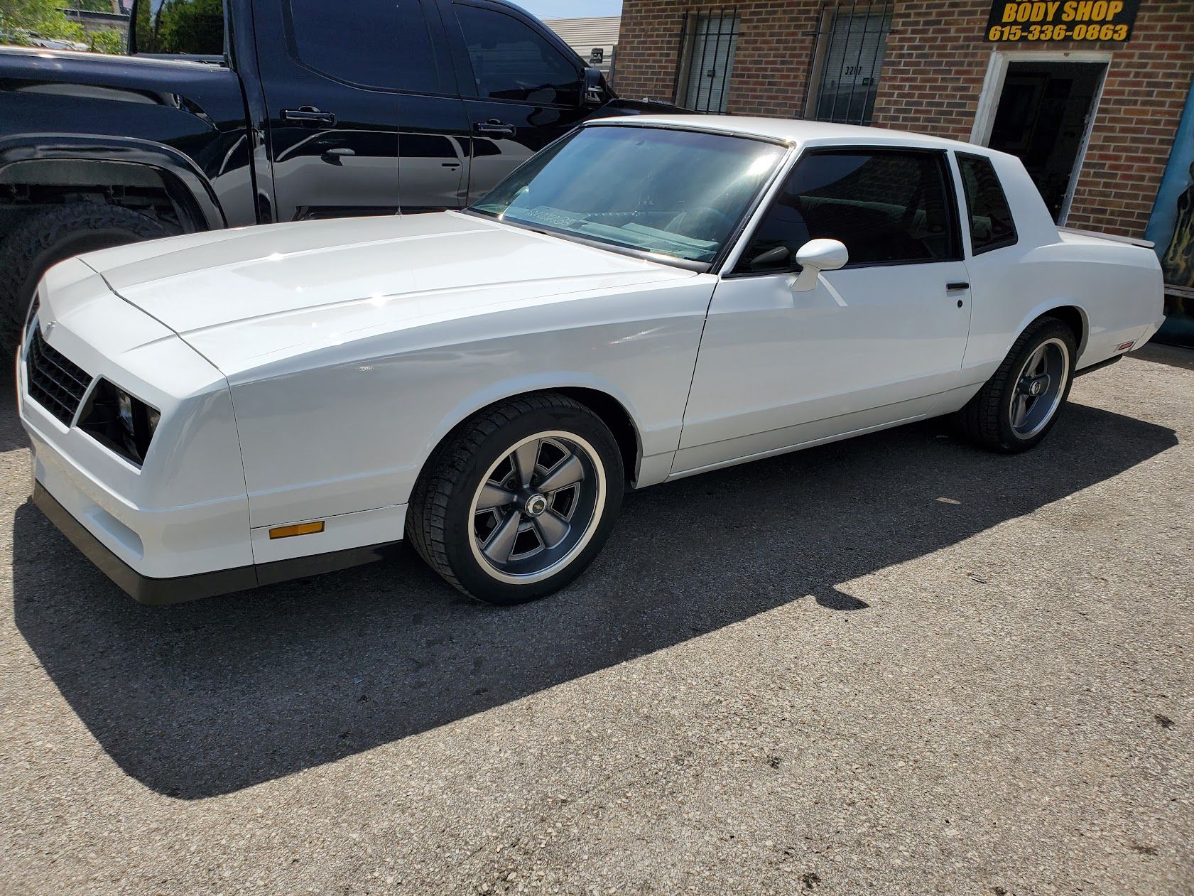 White classic coupe parked on a sunny street beside a black truck