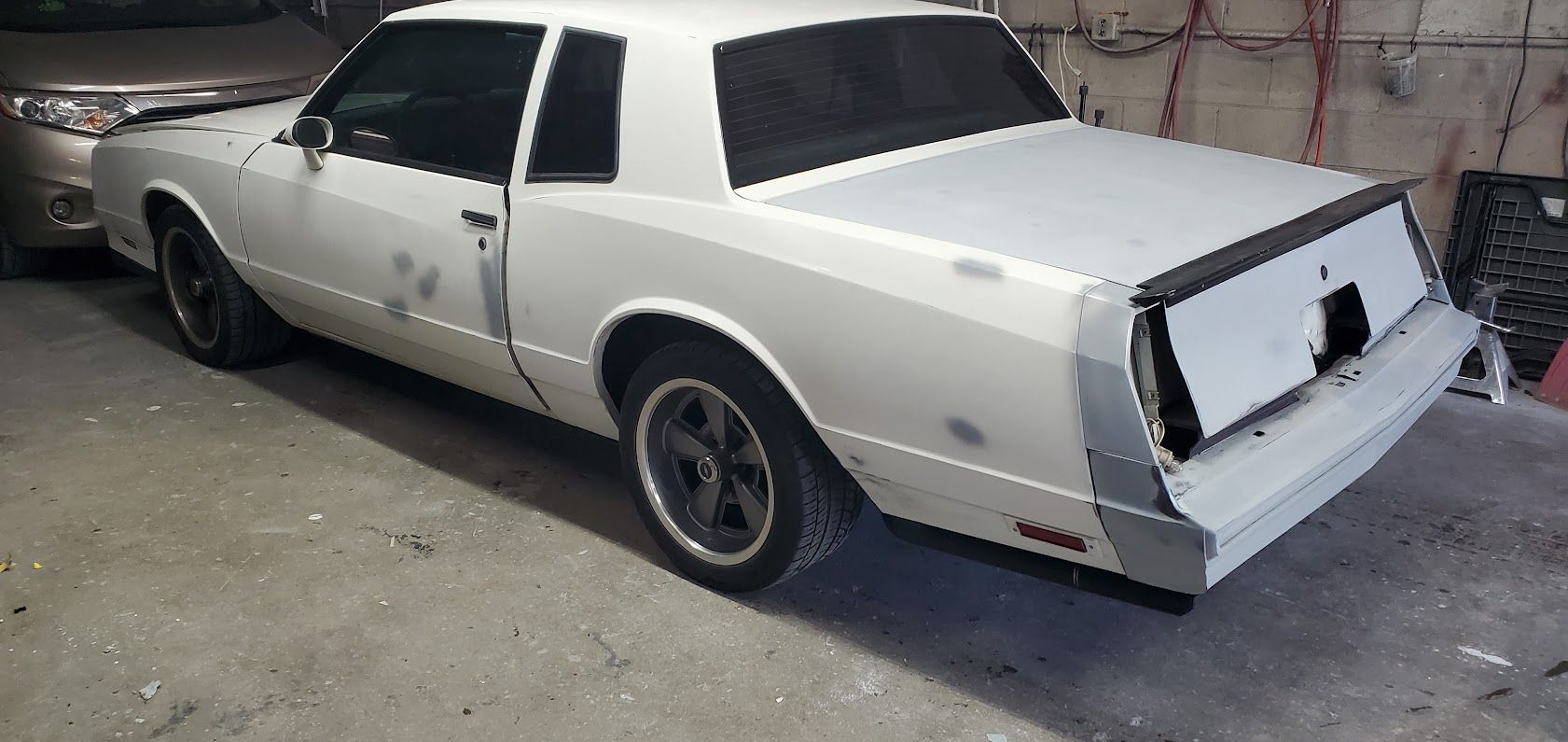White classic sedan parked outdoors with rear damage and missing taillights