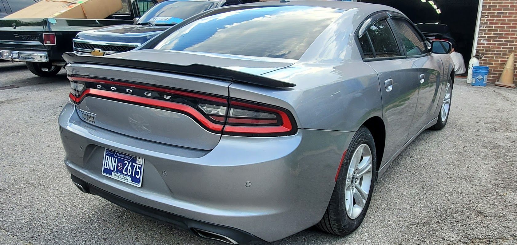 Gray sedan rear view in a parking lot, with a continuous red taillight bar and spoiler.
