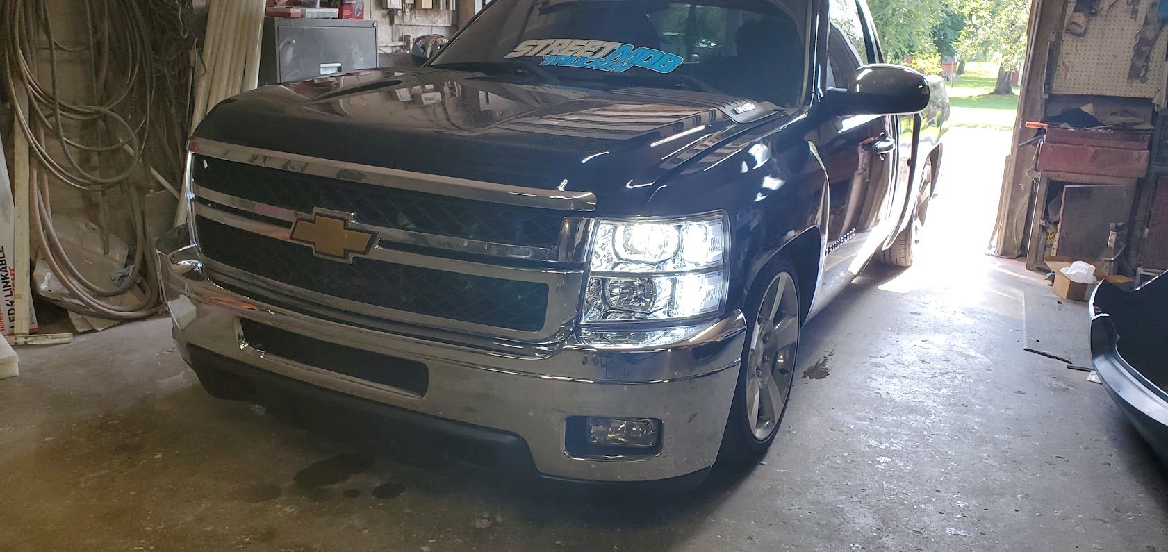 Black Chevrolet pickup truck parked in a dim garage, front view with headlights on