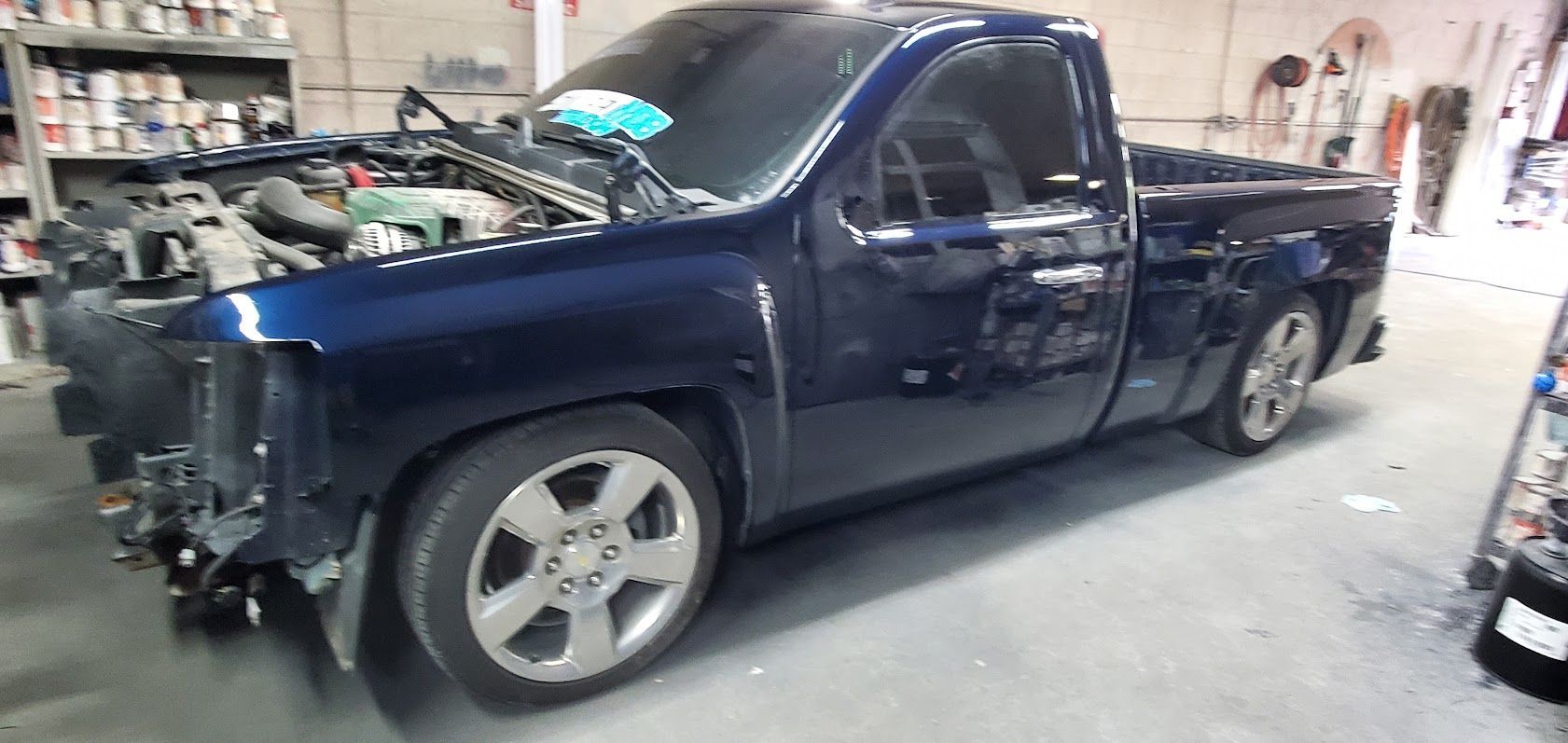 Dark blue pickup truck in a garage, front end disassembled for repairs