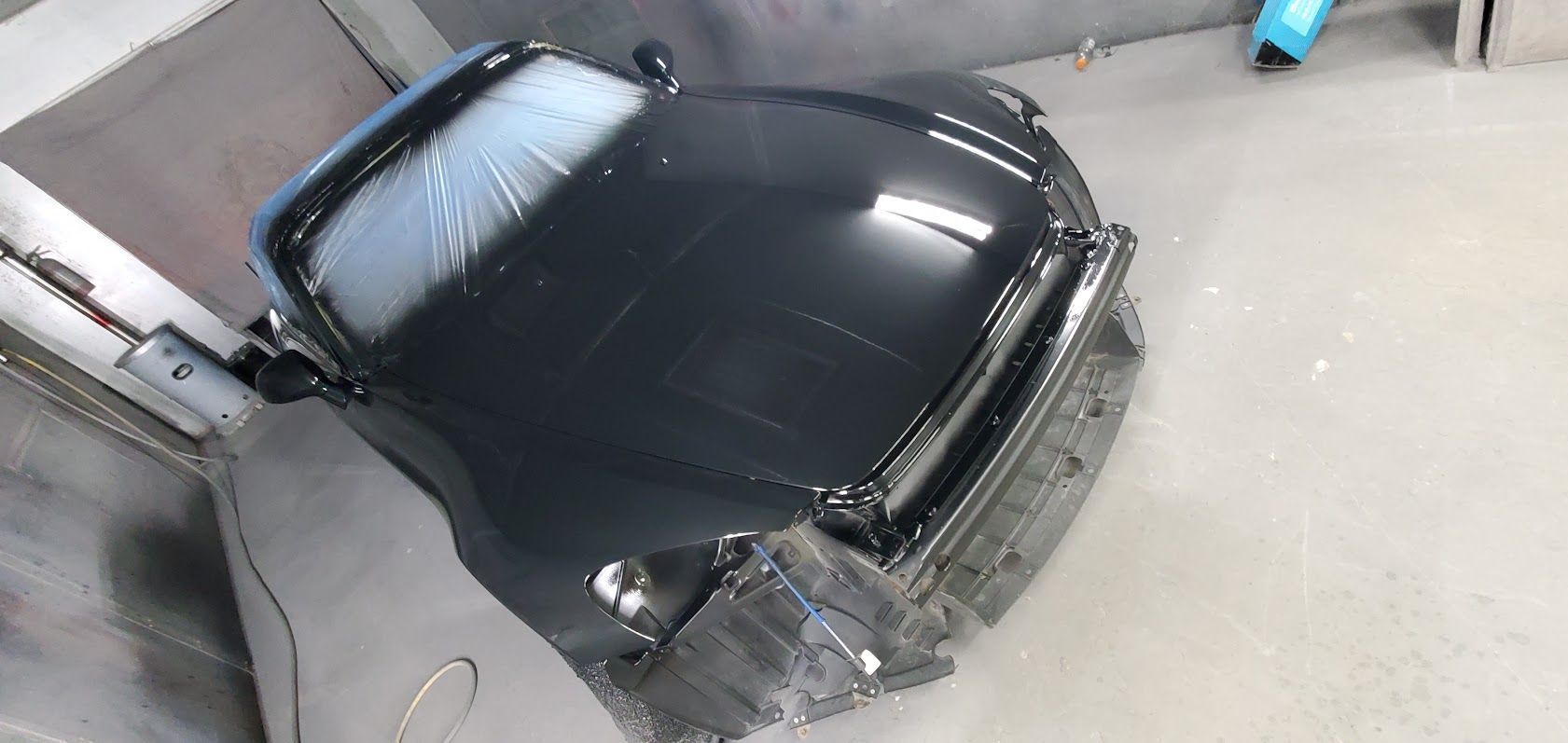 Black car body shell in a workshop, viewed from above with front damage exposed