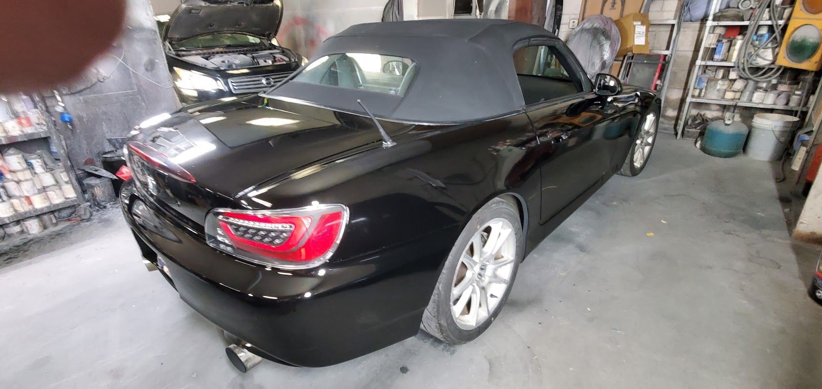 Black convertible sports car parked in a garage, rear view with taillights visible