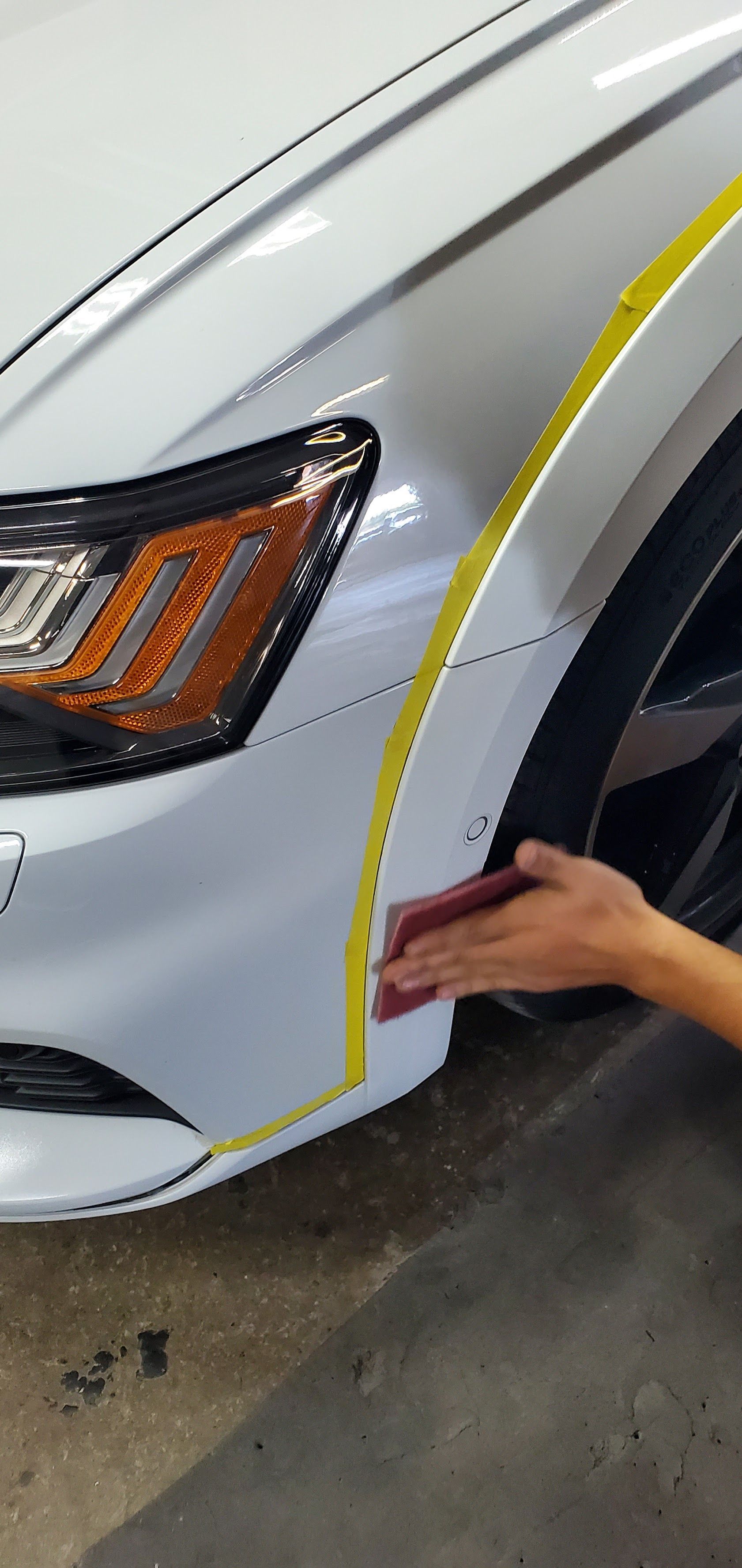 Hand measuring panel gap on white car front fender with yellow masking tape