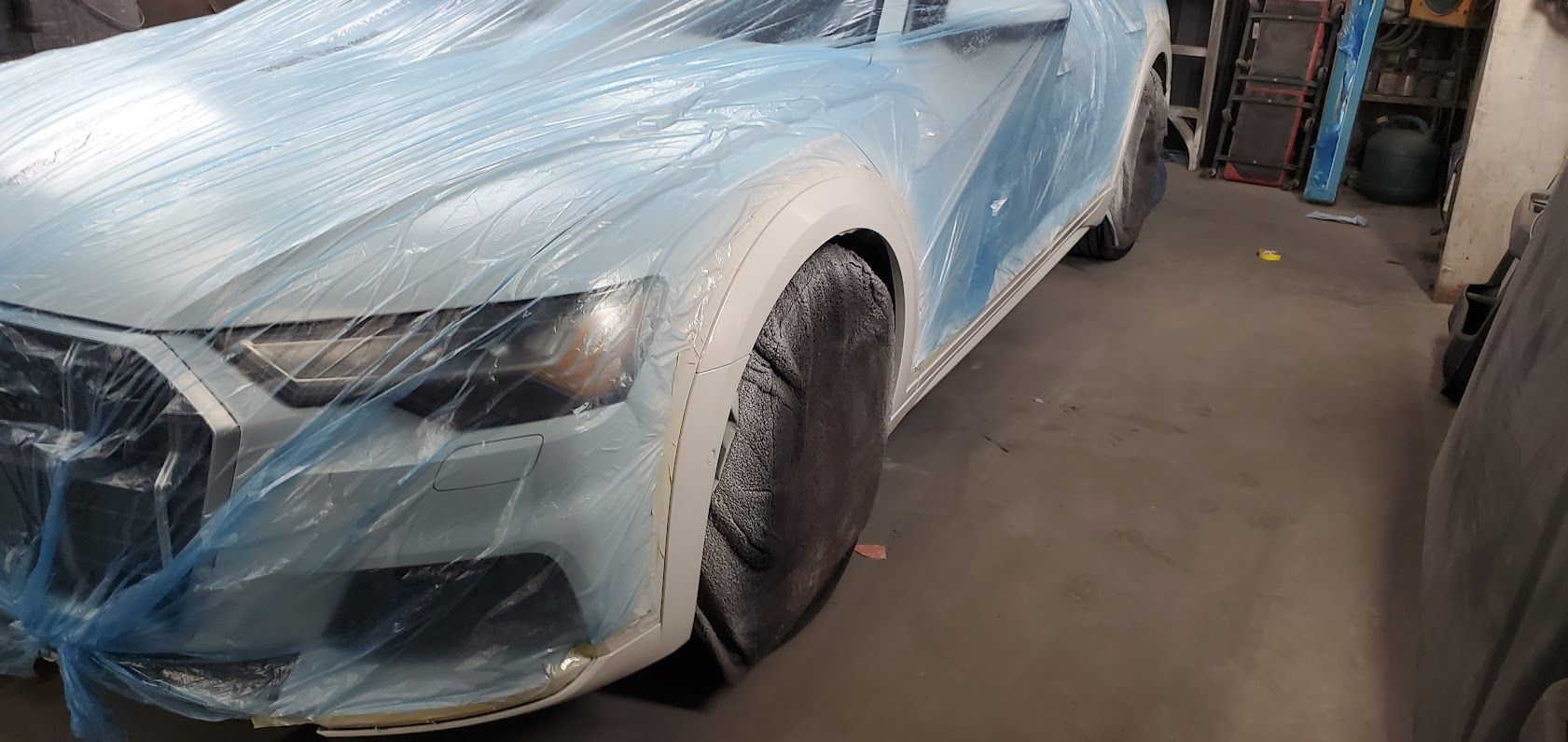Blue car covered in plastic wrap inside a garage, with the front wheel visible