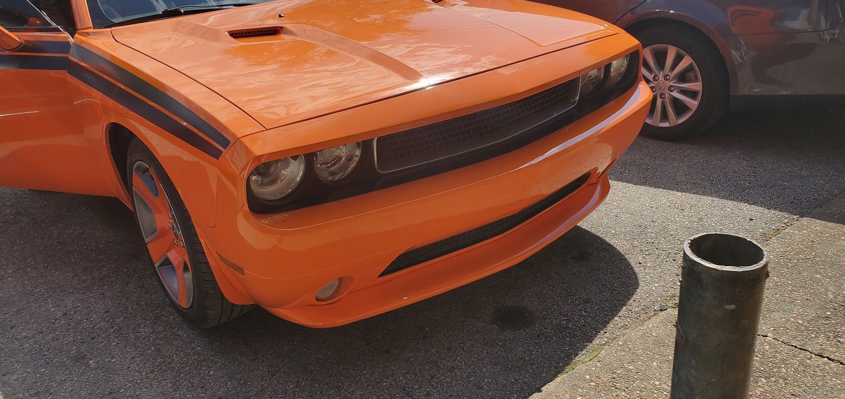 Orange Dodge Challenger parked on a sunny street with a dark car beside it.