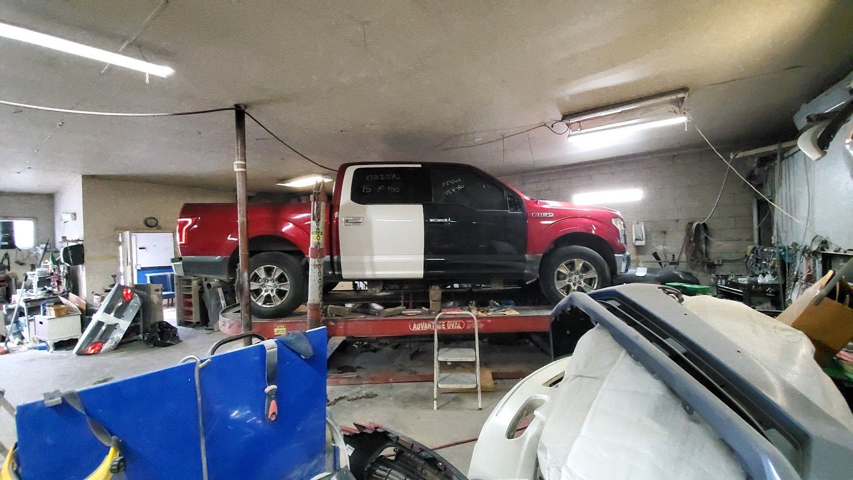 Red and black pickup truck elevated in a cluttered auto repair garage with tools and equipment around it
