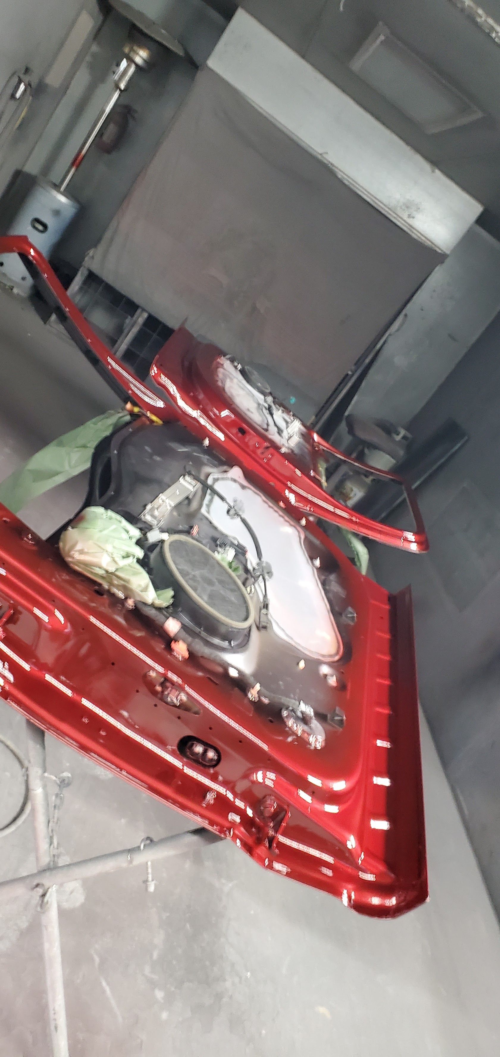 Red car body panel with exposed engine parts inside a gray workshop or garage.