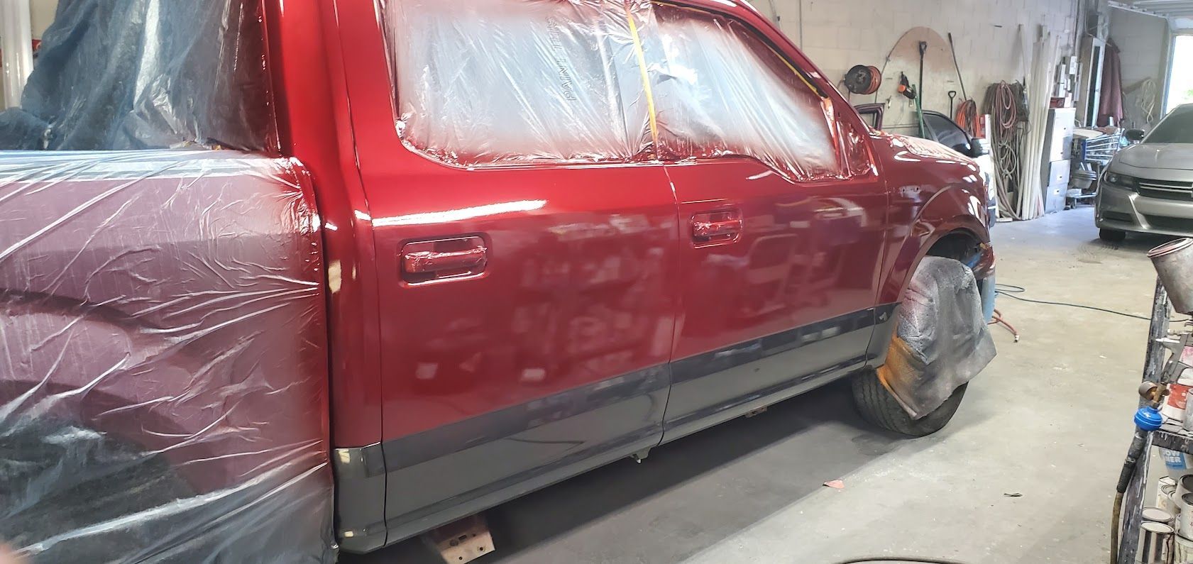 Red pickup truck covered in plastic sheeting inside a workshop, being painted or repaired