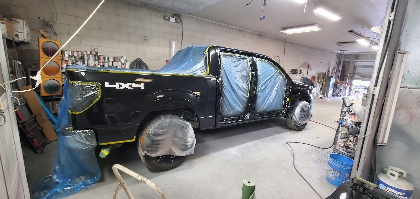 Black car wrapped in blue film in a garage, with wheels covered and tools nearby