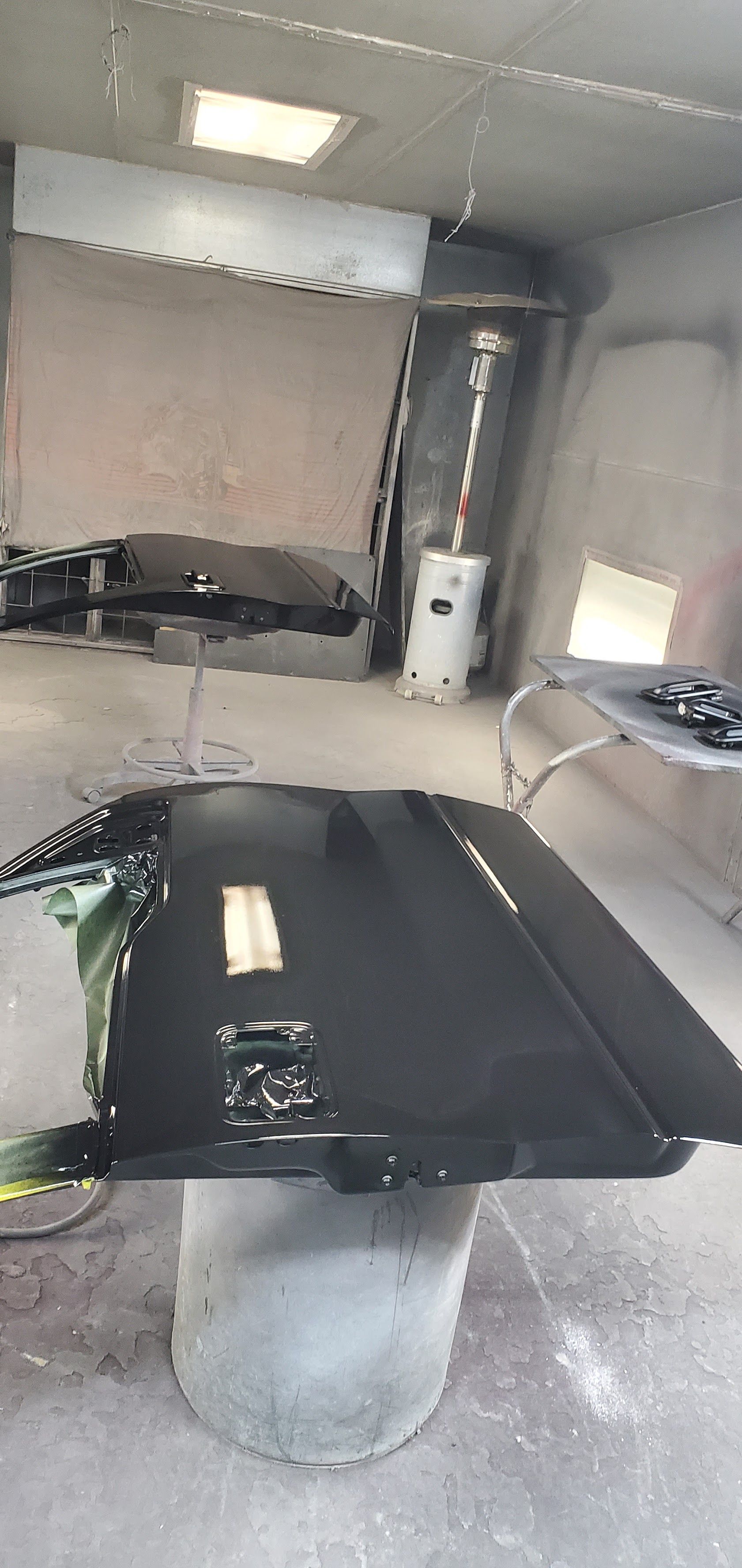 Small garage with a black car hood open over an engine bay and a water heater in the back corner.