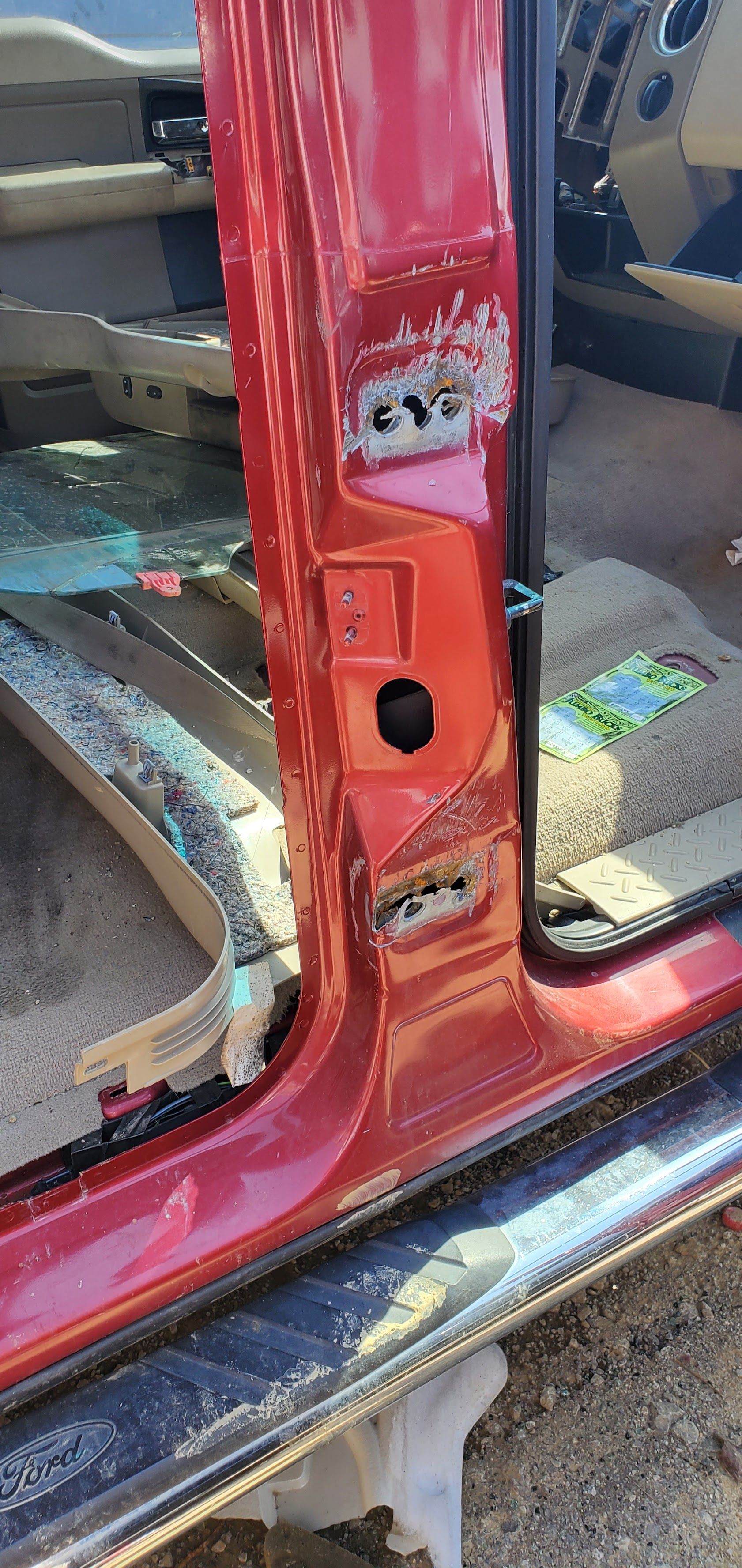 Close-up of a red car door frame with a damaged rocker panel and exposed metal.