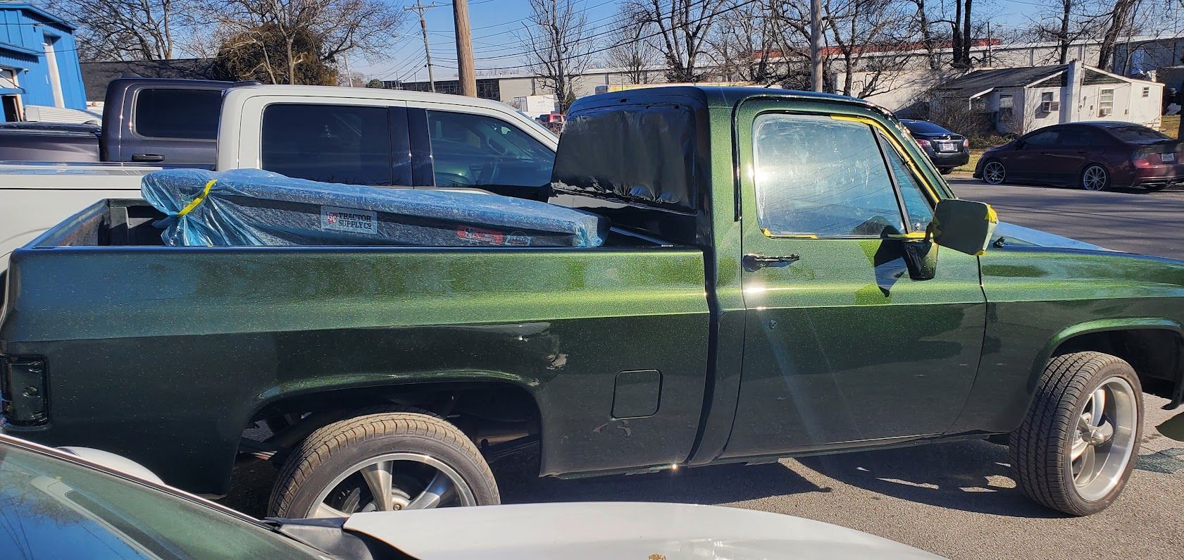 Green pickup truck parked on a street with a blue pickup bed cover in winter sunlight