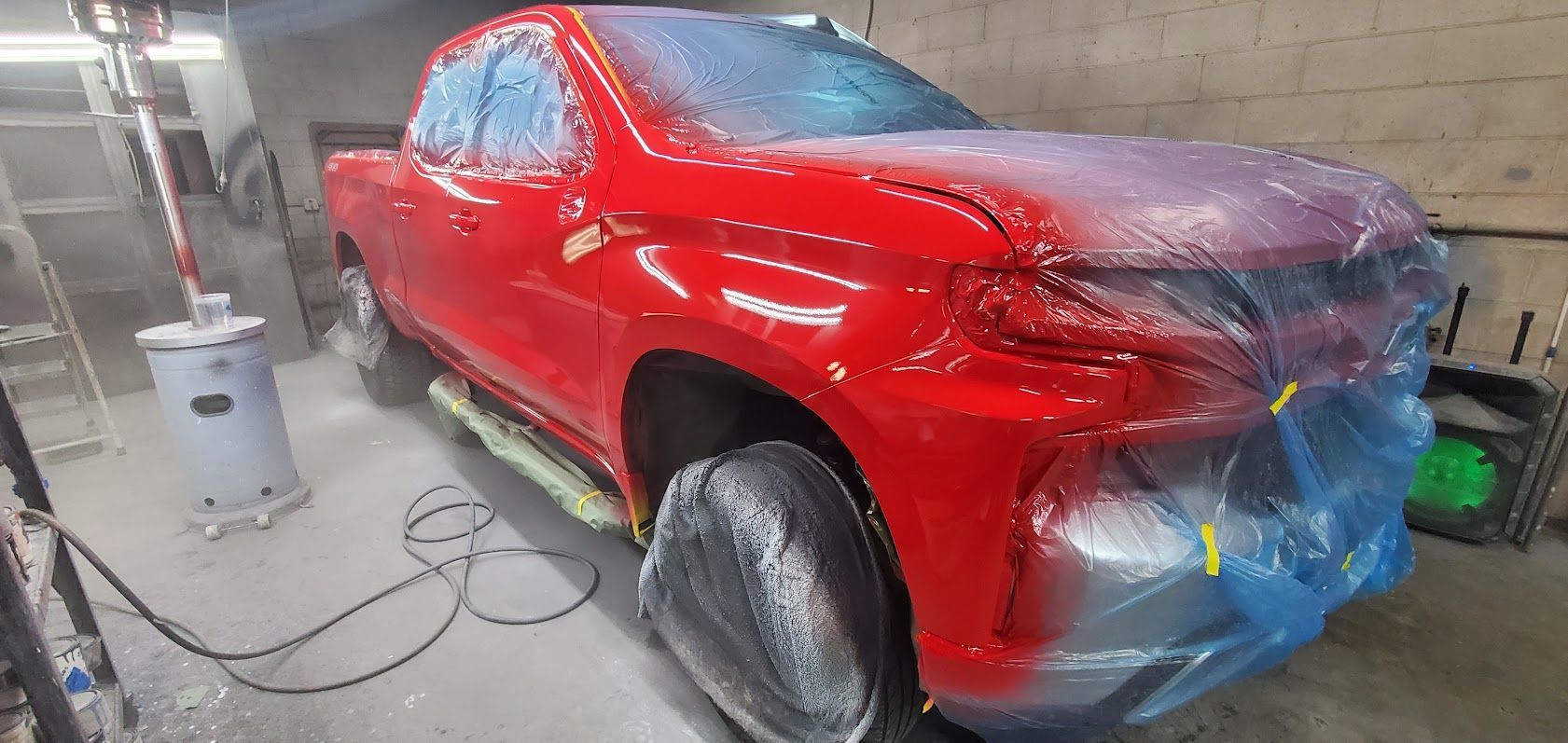 Red SUV being spray painted in a workshop, with a masked rear and paint equipment nearby.