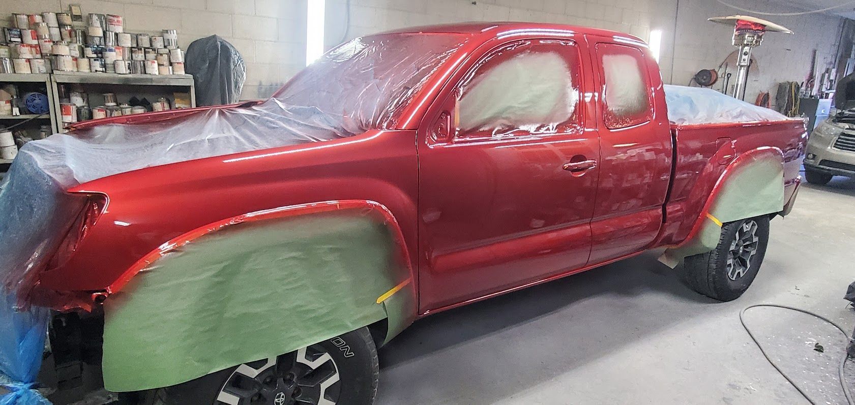 Red pickup truck in a workshop, partially painted with green primer on the front and rear panels.