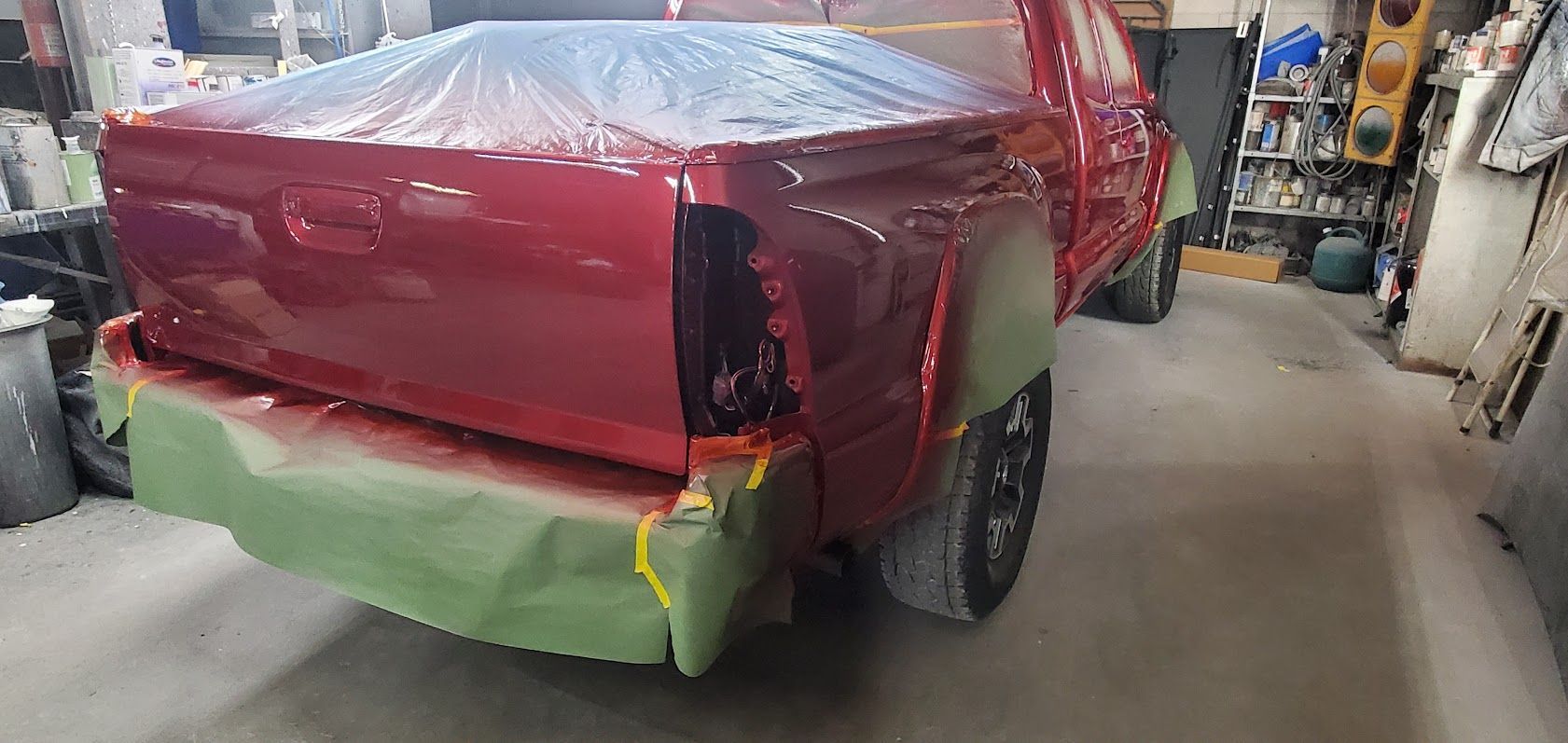 Red pickup truck in a workshop, rear end covered with masking plastic and paint being repaired