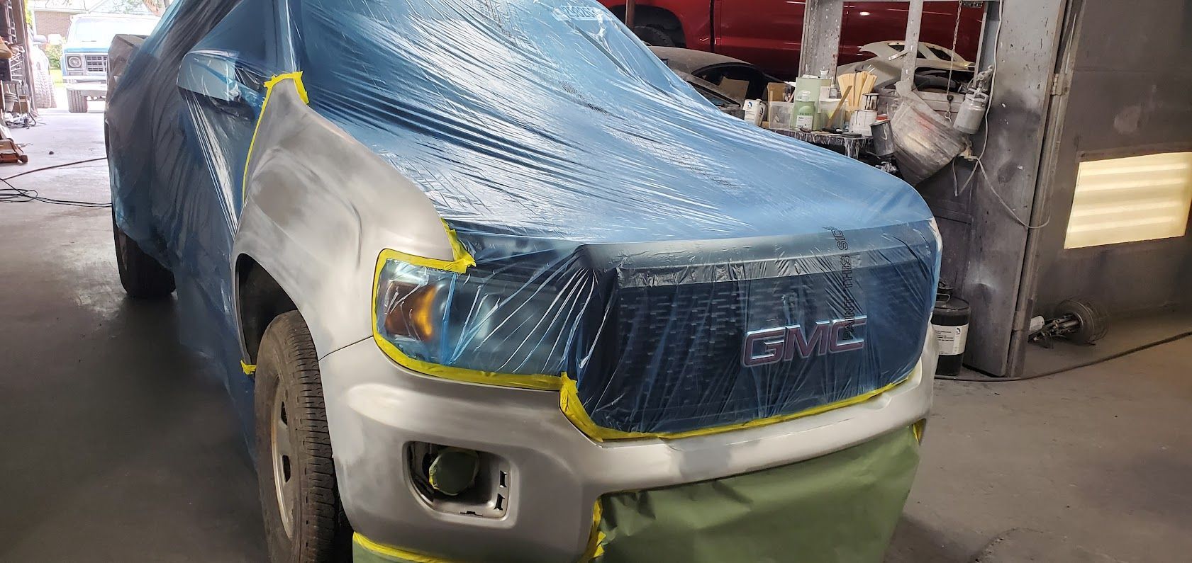 SUV in a repair shop, front end wrapped in blue protective plastic and a green bumper cover installed