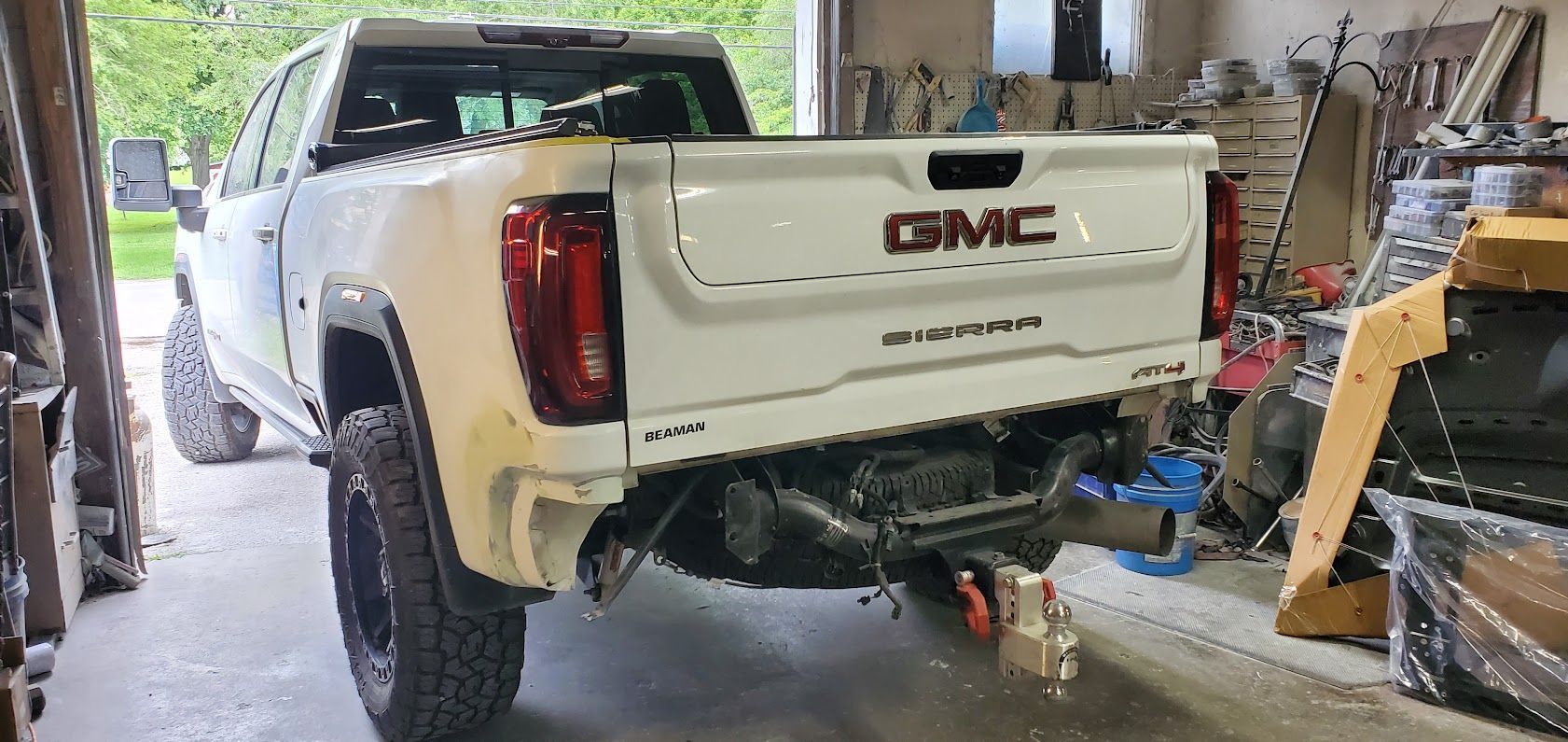 White GMC pickup in a garage, rear bumper removed and tools/equipment around it.