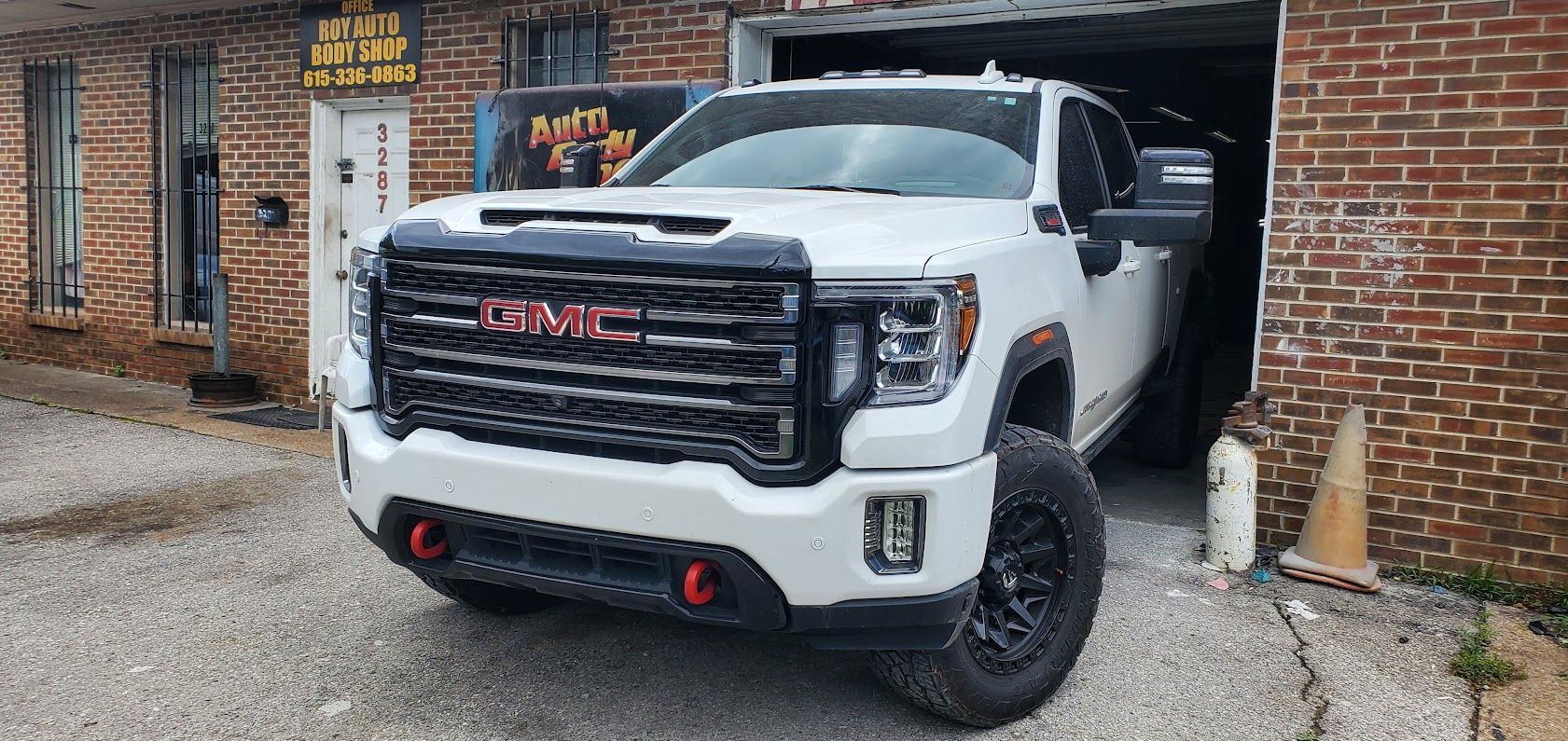 White GMC truck parked partly in a brick garage, front facing with red tow hooks.