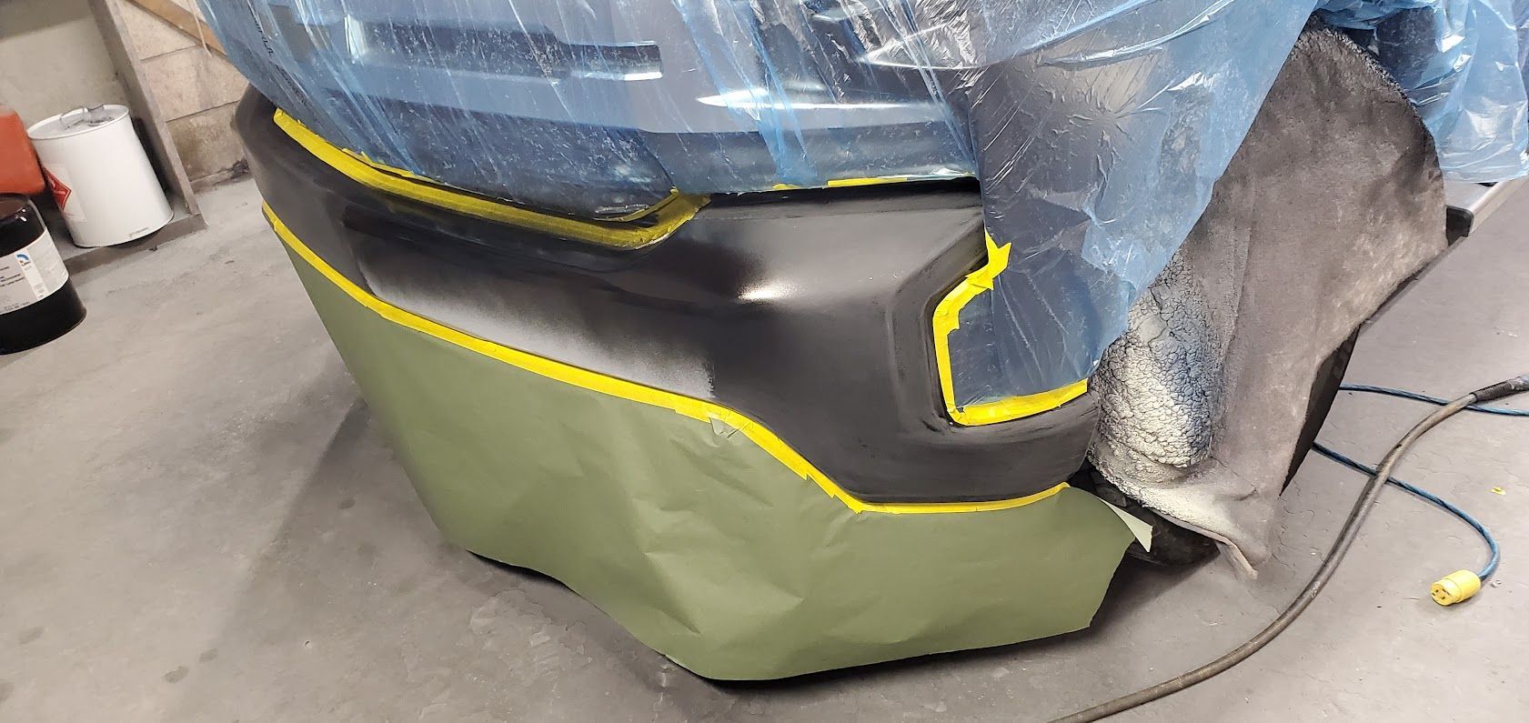 Car wrapped in blue and green protective film with yellow tape in a workshop.