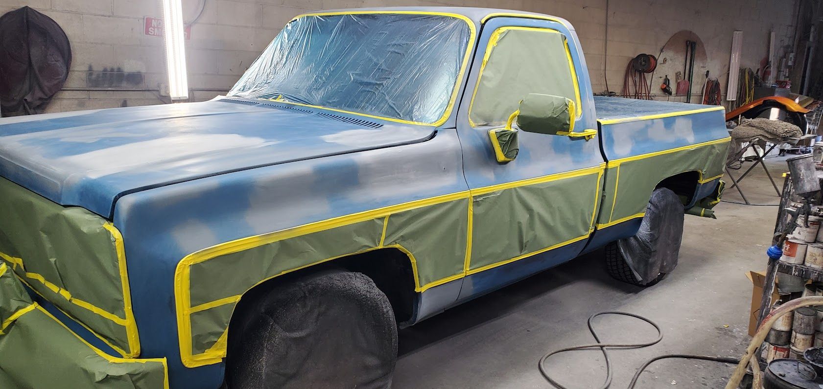 Old blue pickup truck in a garage, masked with yellow tape and paper for painting