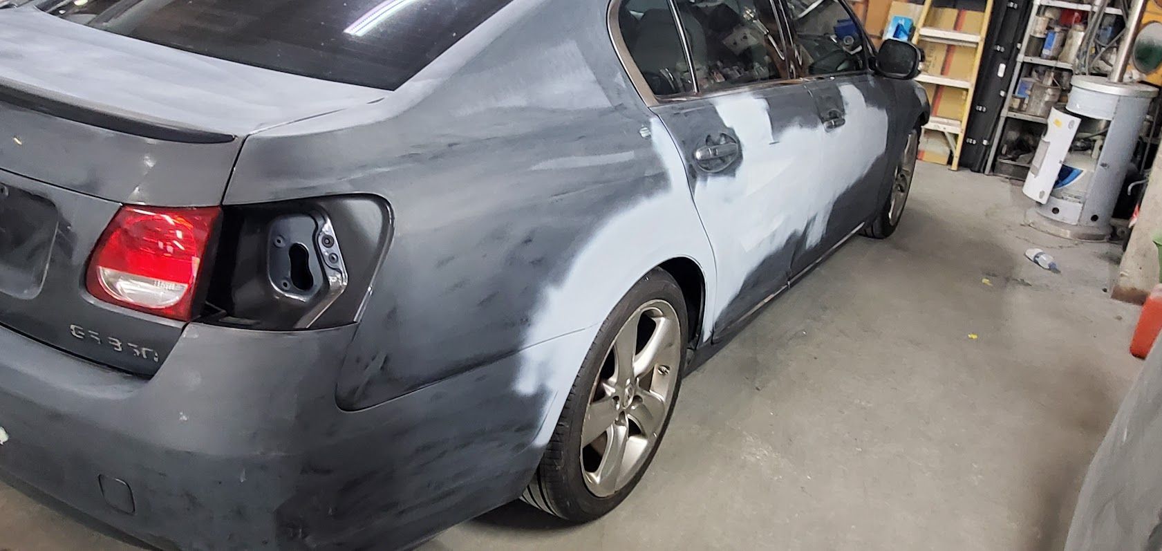 Gray car in a garage, rear side damaged with black primer and missing rear light area.