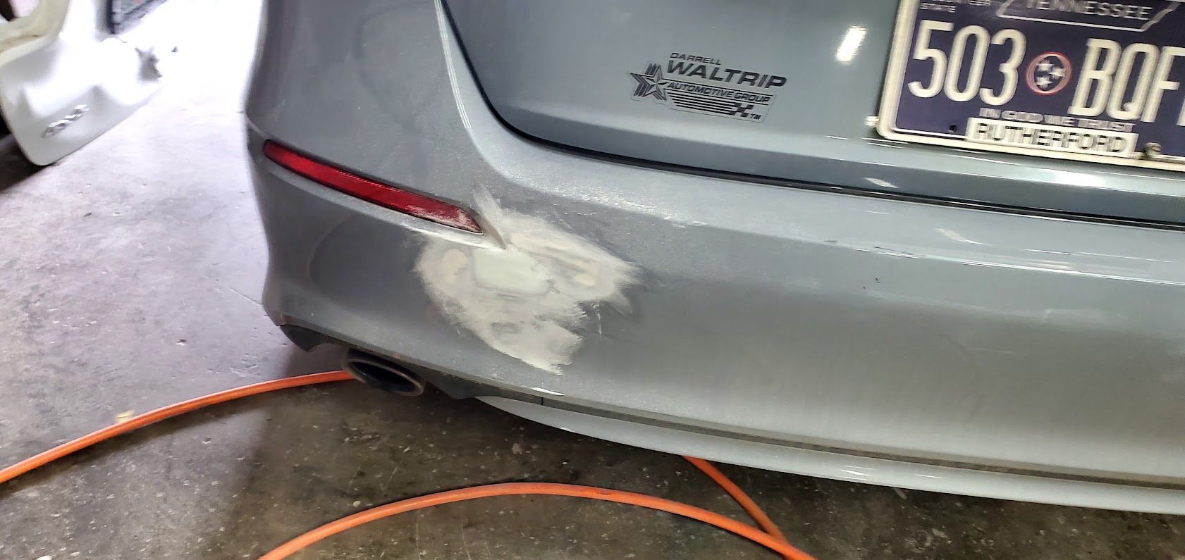 Rear of a silver car with a white scuff on the bumper, garage floor and orange hose visible.